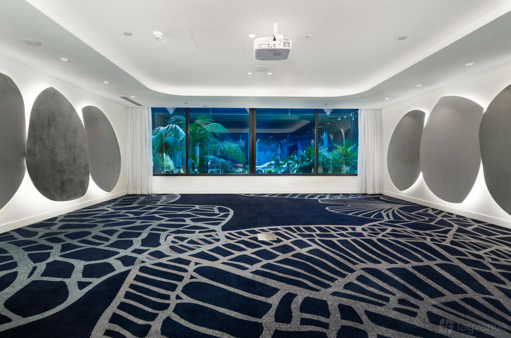 A meeting room with geometric carpet, round acoustic panels on the walls, and large windows overlooking greenery at West Hotel Sydney.