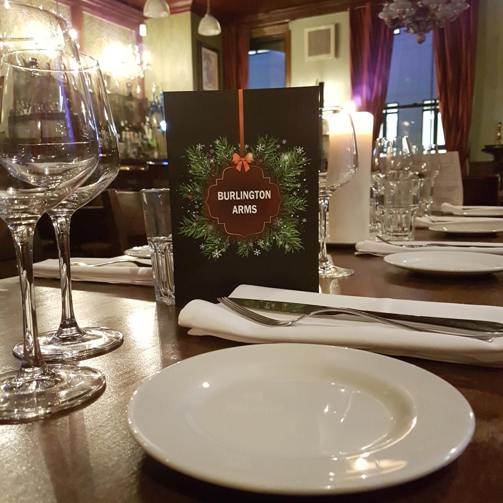 A pub table set with white plates, wine glasses, and a holiday-themed menu at The Burlington Arms