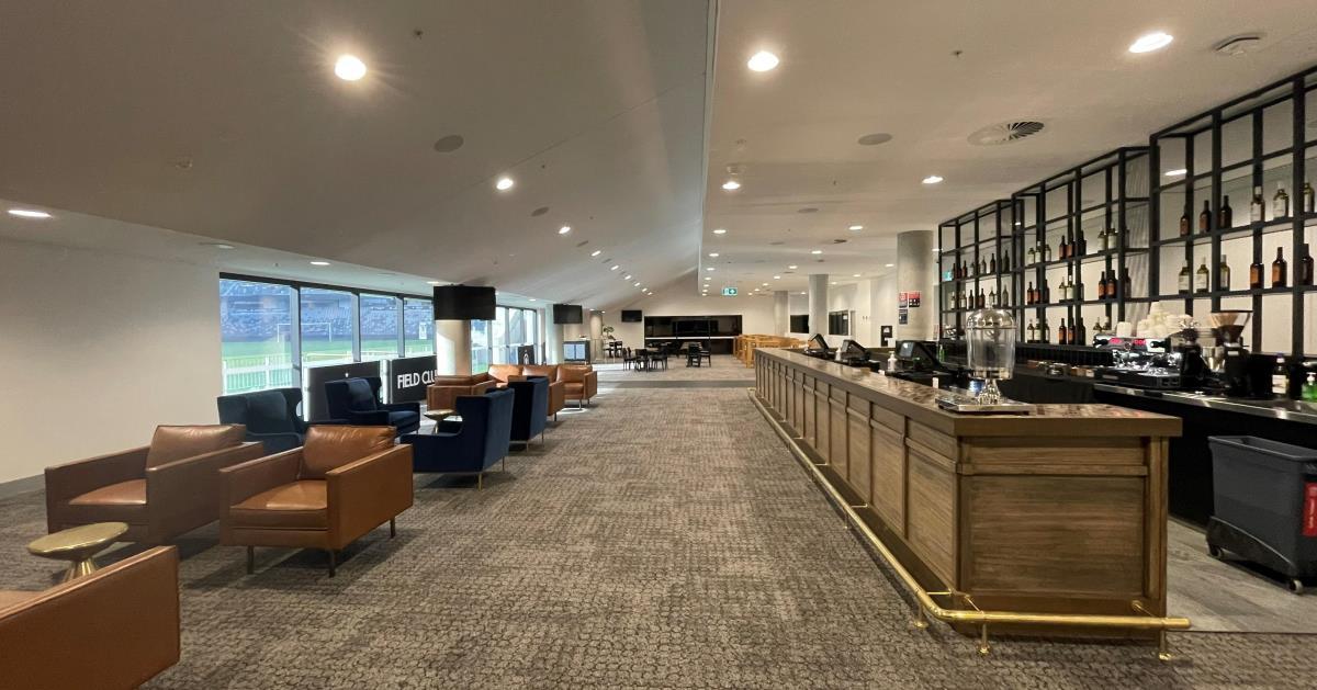 An event space with floor-to-ceiling windows, lounge seating, and a long bar at CommBank Stadium.
