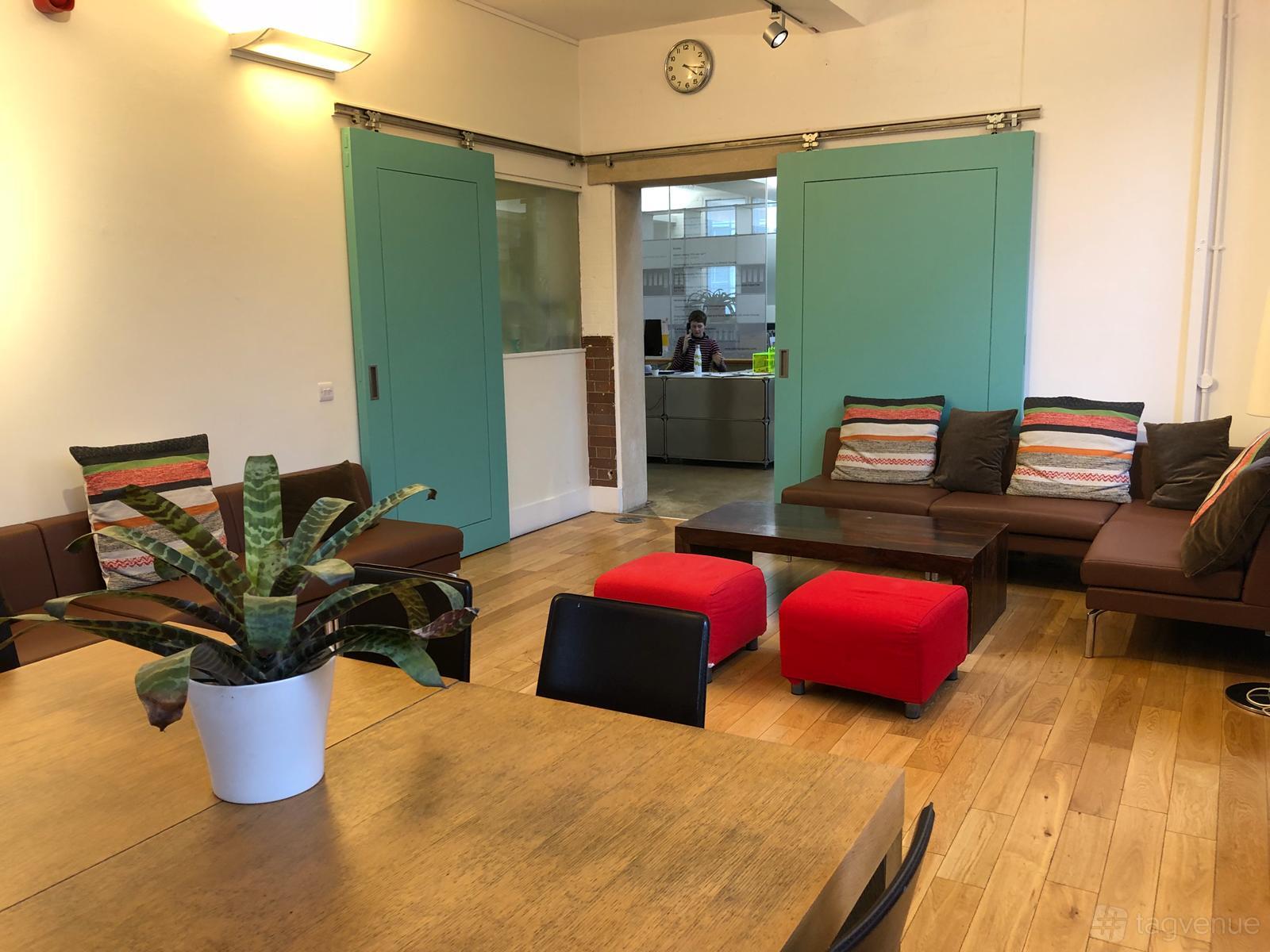 A meeting room with colorful sofas, red ottomans, wooden floors, and a potted plant on a table at Siobhan Davies Dance Studios.