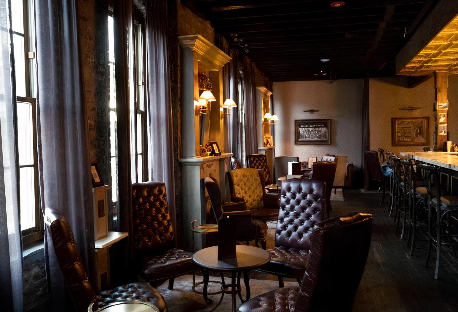A cocktail bar with tufted leather chairs, tall windows with sheer curtains, and wall sconces at The Marble Ring.