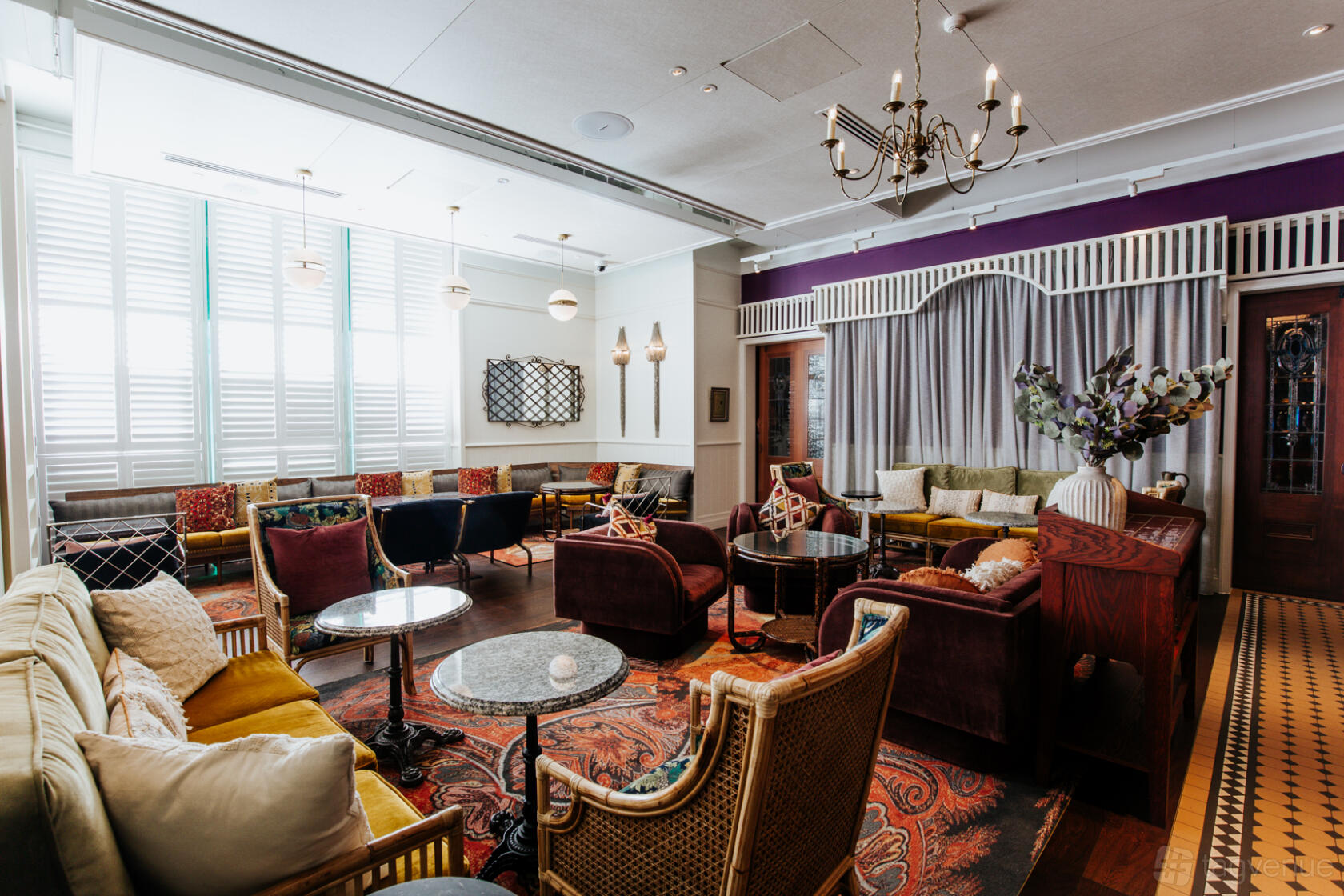 An event space with plush armchairs, patterned rugs, and natural light through shuttered windows at Ovolo The Valley.