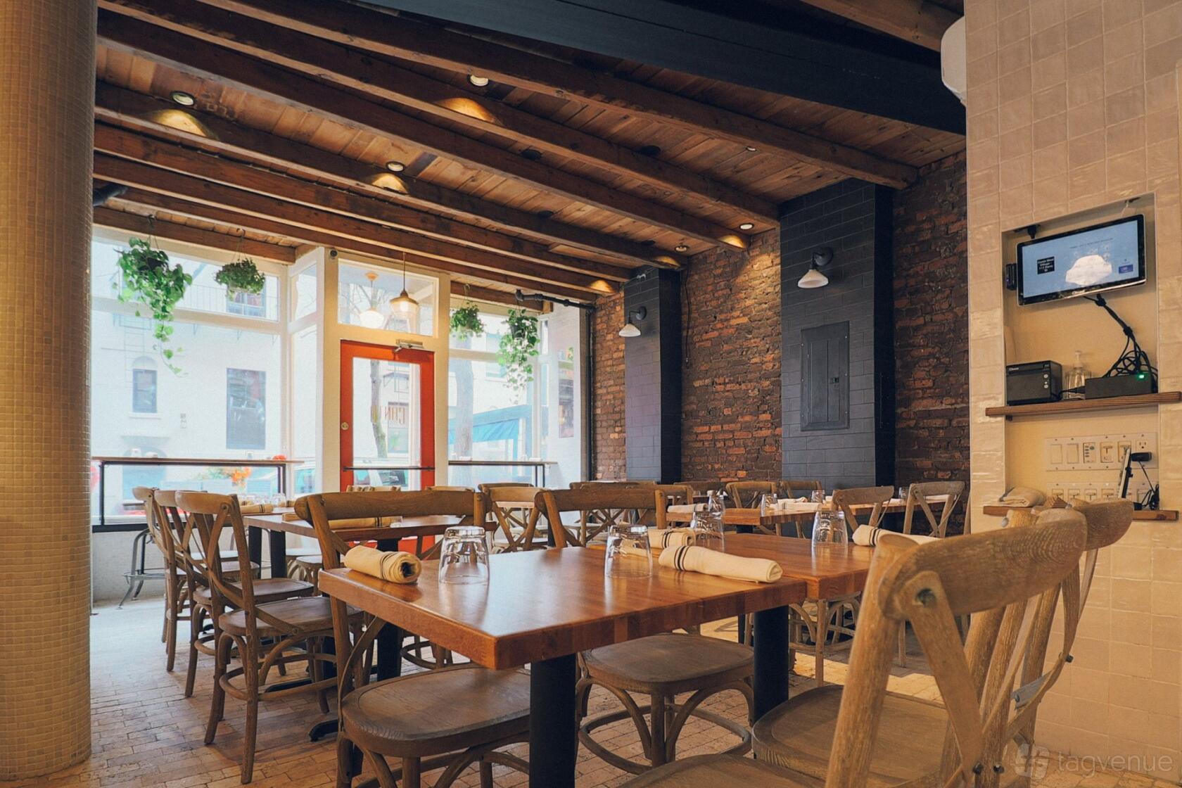 A restaurant with wooden beams, exposed brick walls, large windows, and hanging plants at Canto.