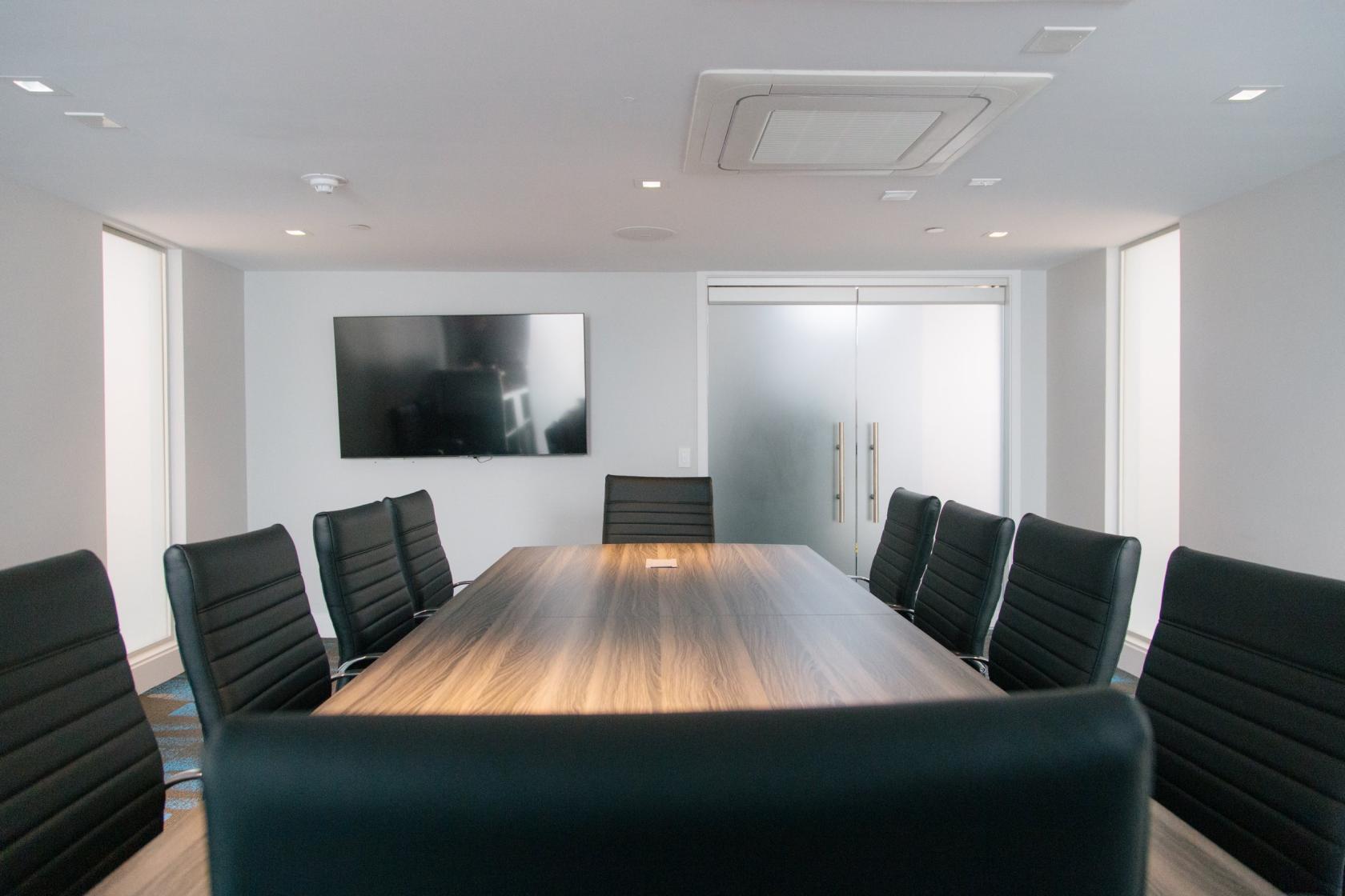A boardroom with a long wooden conference table, black leather chairs, and a wall-mounted screen at H2O Hermosa.