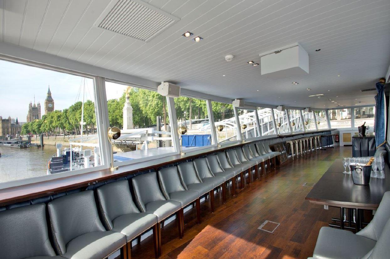 An event space on a boat with wraparound windows, river views, and rows of gray chairs at The Tattershall Castle.