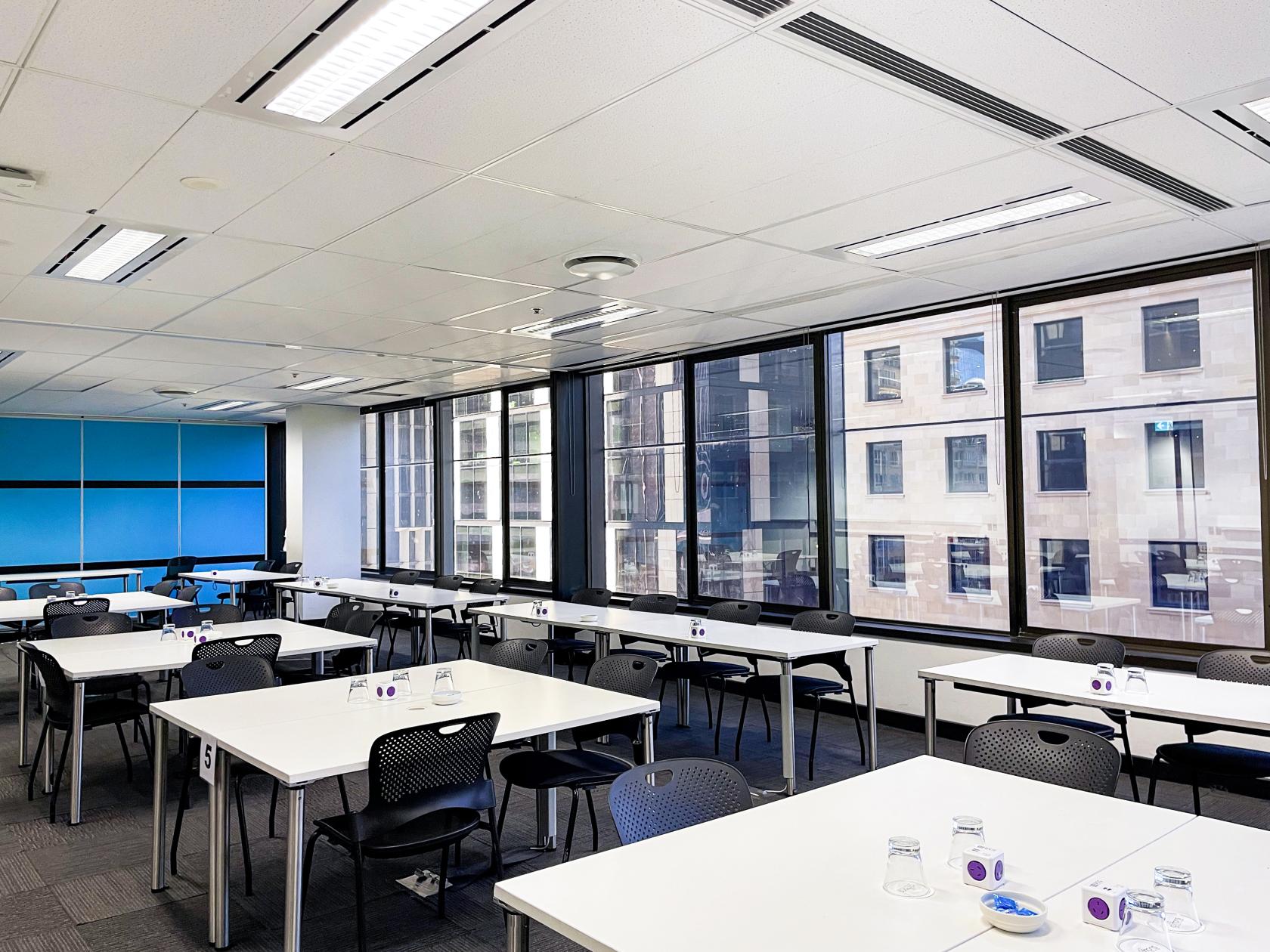 An event venue with large windows, white tables, black chairs, and bottled water at Cliftons Canberra – Moore St.