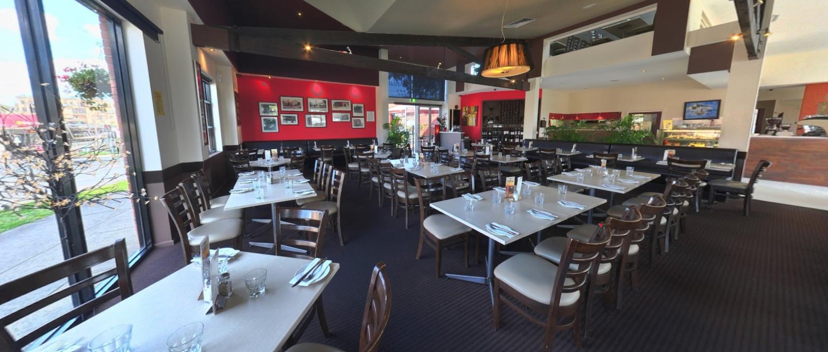 A restaurant dining area with wooden chairs, square tables, red accent walls, and wall art at Vibrante Restaurant.