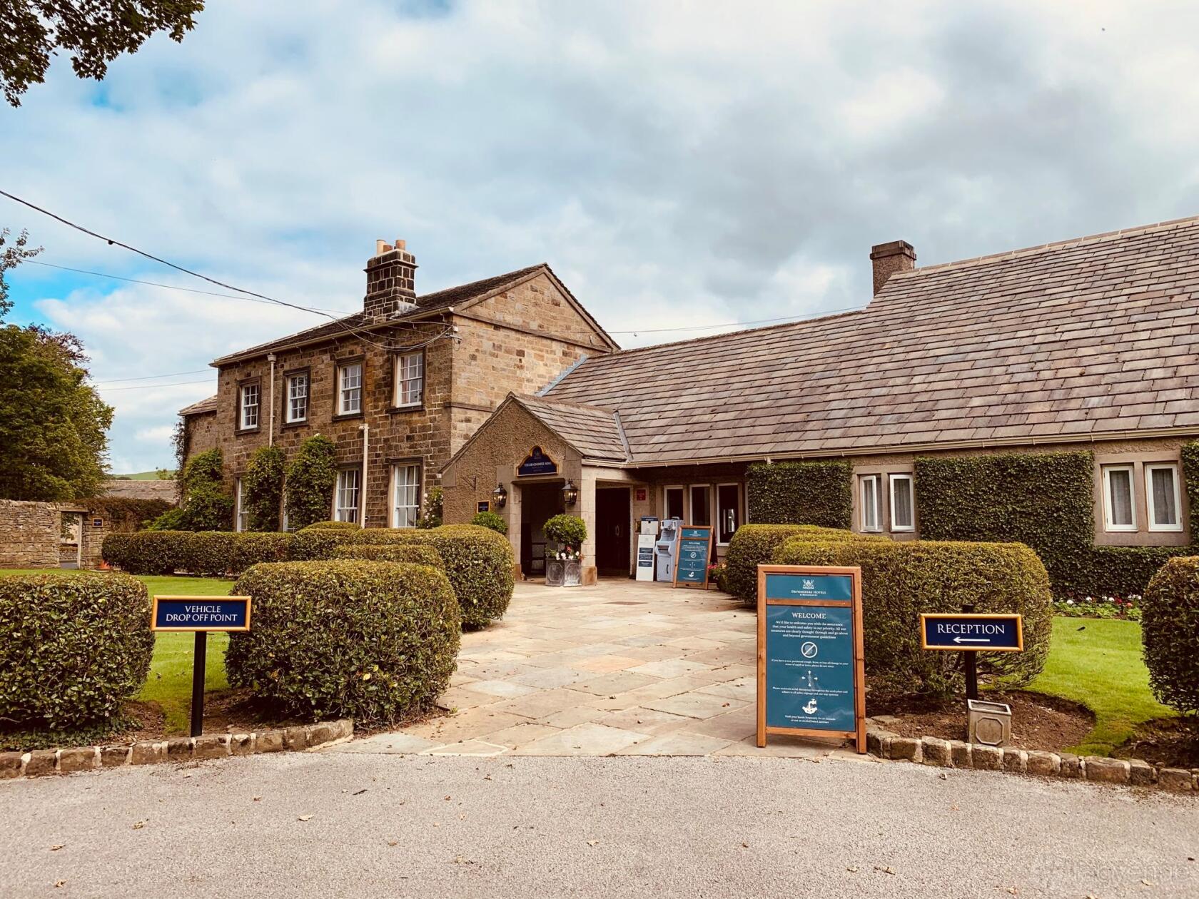 A hotel with stone buildings, manicured hedges, and a paved entrance at Devonshire Arms Hotel & Spa.