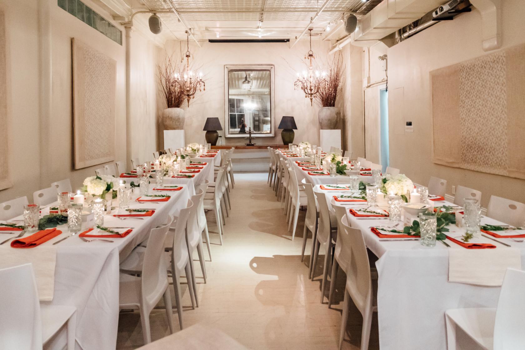 A loft with long banquet tables covered in white linens, floral centerpieces, and candles at The Sixth Floor Loft.