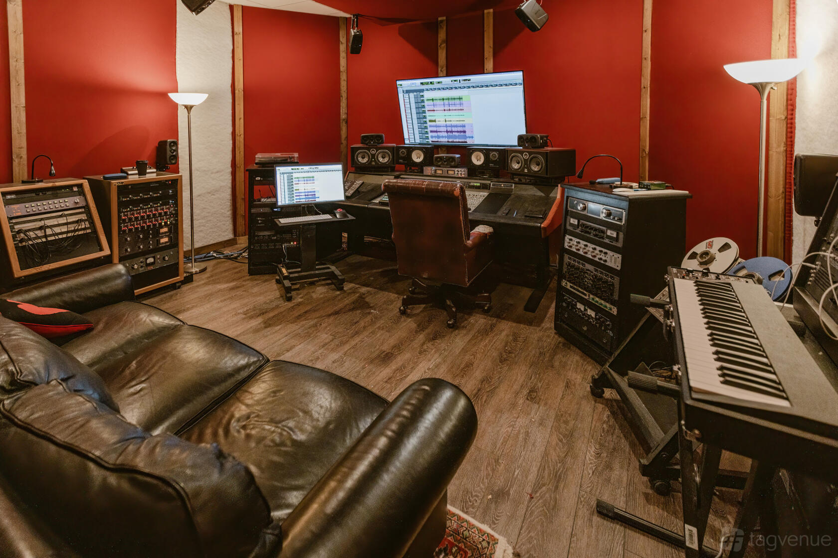 A recording studio with red acoustic panels, mixing console, sofa, and keyboard at Nomad Recording Studio.
