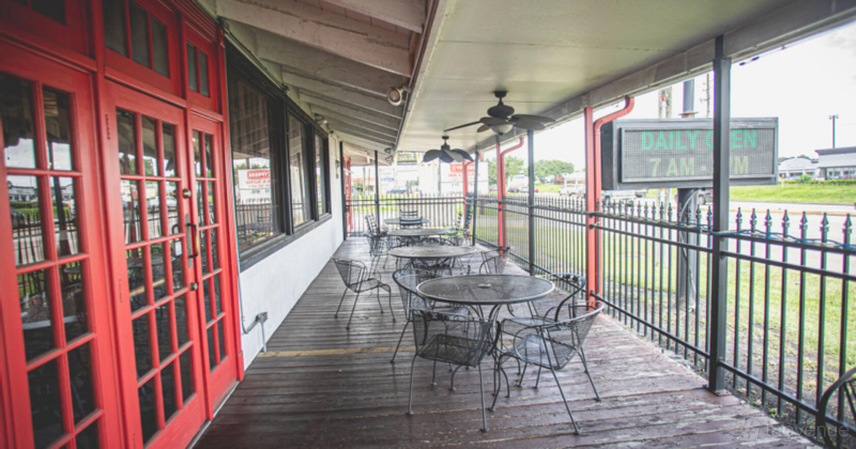 A covered terrace with metal patio tables, chairs, ceiling fans, and a wooden floor at Victor's Restaurant.