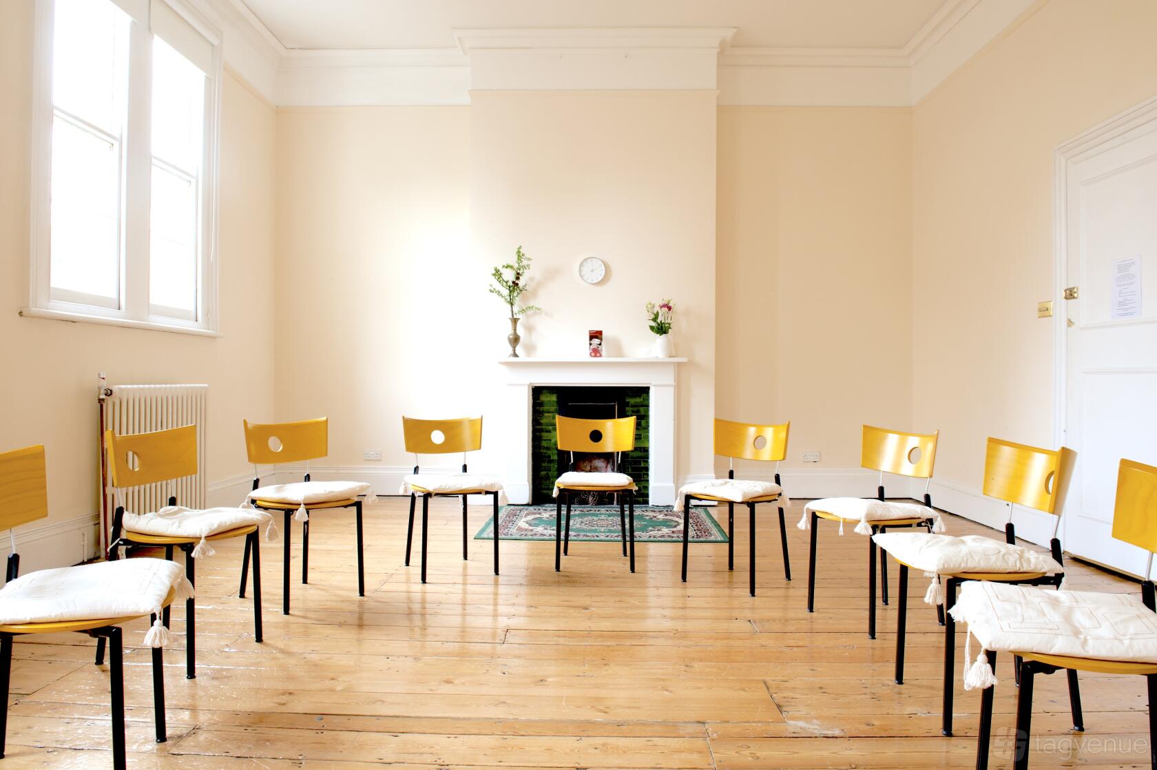 An event space with a circle of wooden chairs, natural light, and a decorative fireplace at Jamyang Buddhist Centre.