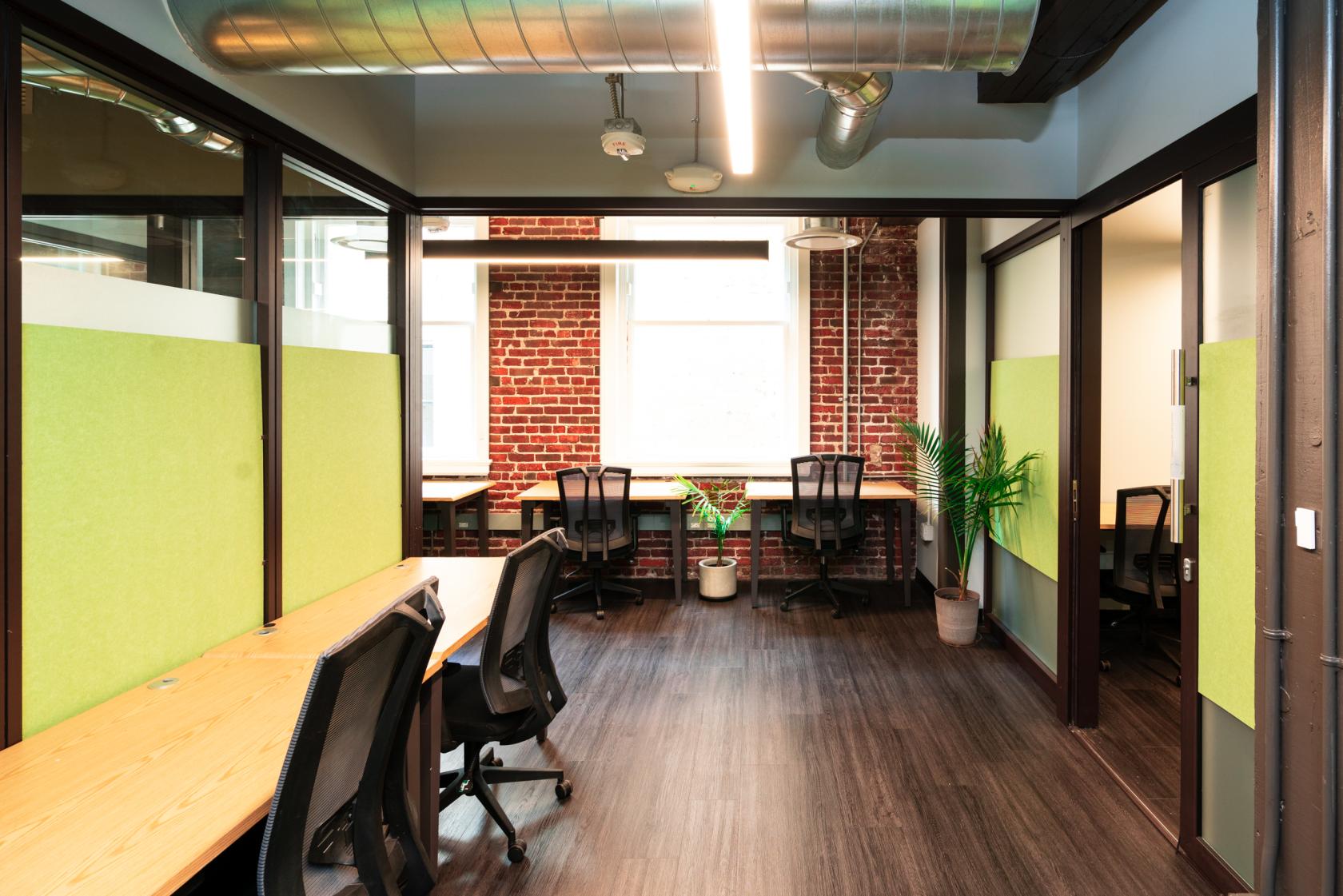 An office space with exposed brick walls, large windows, shared desks, and office chairs at Werqwise San Francisco.