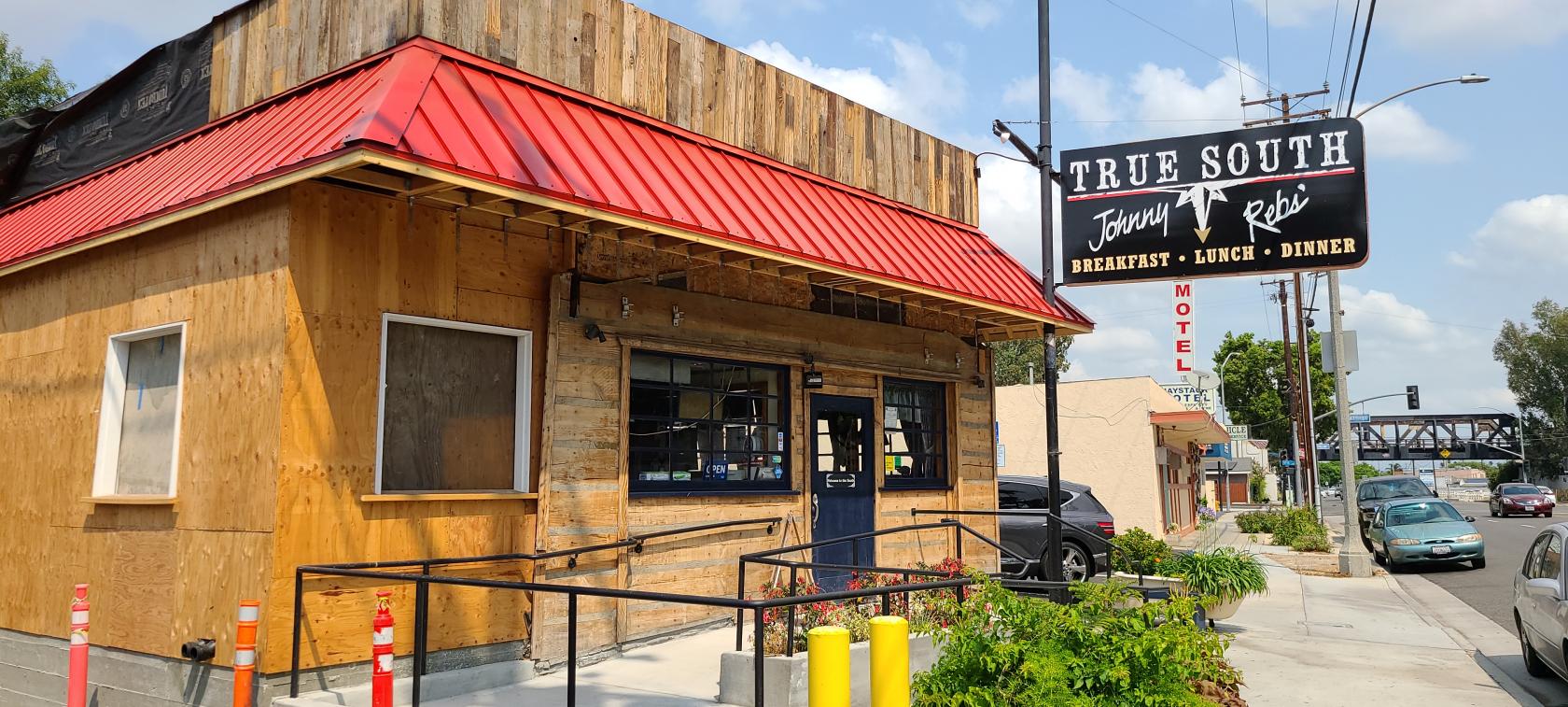 A restaurant with a rustic wood exterior, red metal roof, and large street sign at Johnny Rebs' True South.