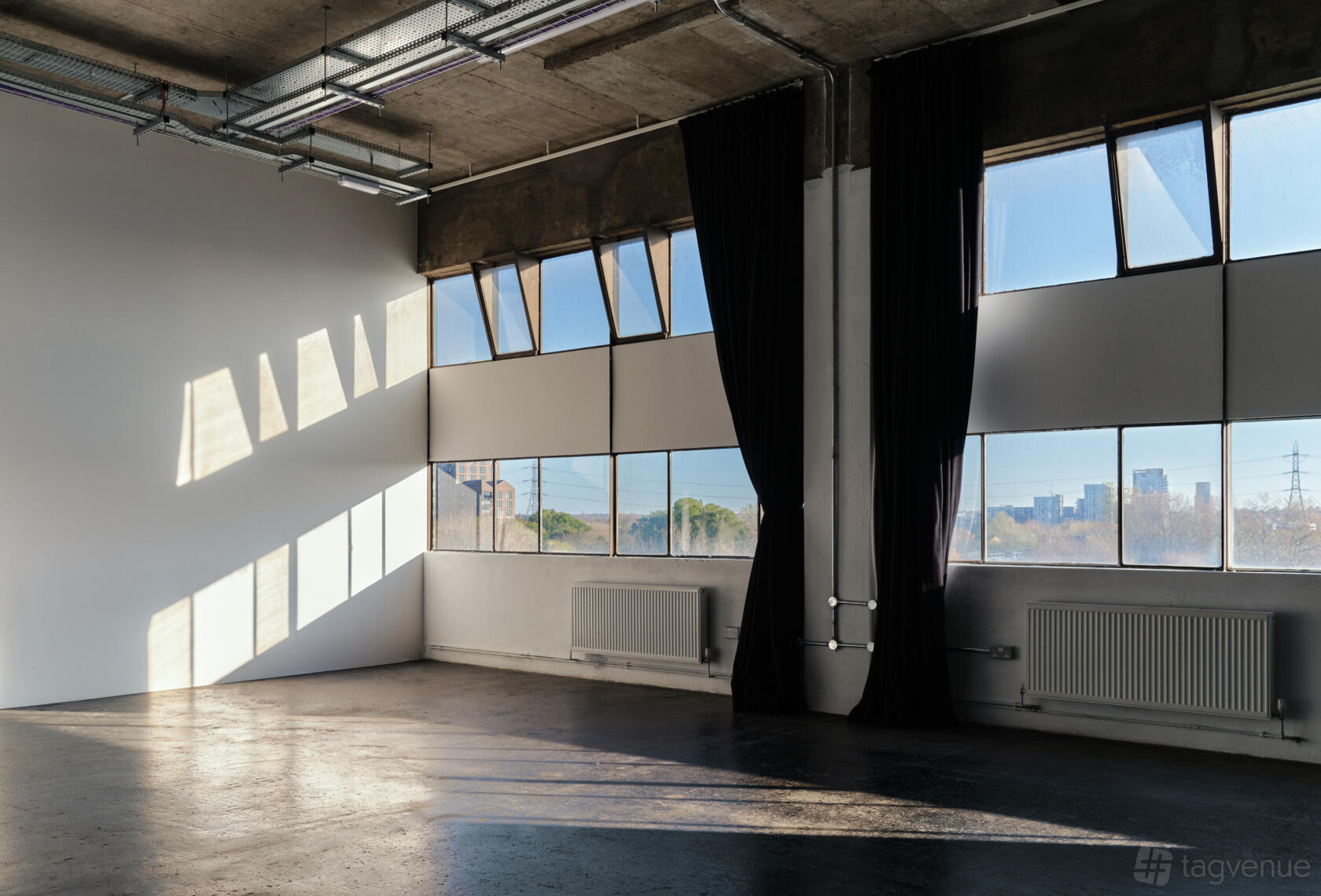 A photo studio with large industrial windows, polished concrete floors, and black-out curtains at Studio Monde.