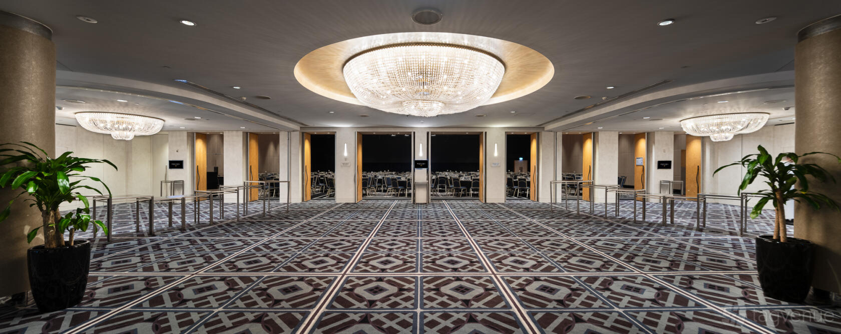 An event space in a hotel with a large geometric carpet, mirrored walls, and a crystal chandelier at Sofitel Sydney Wentworth.