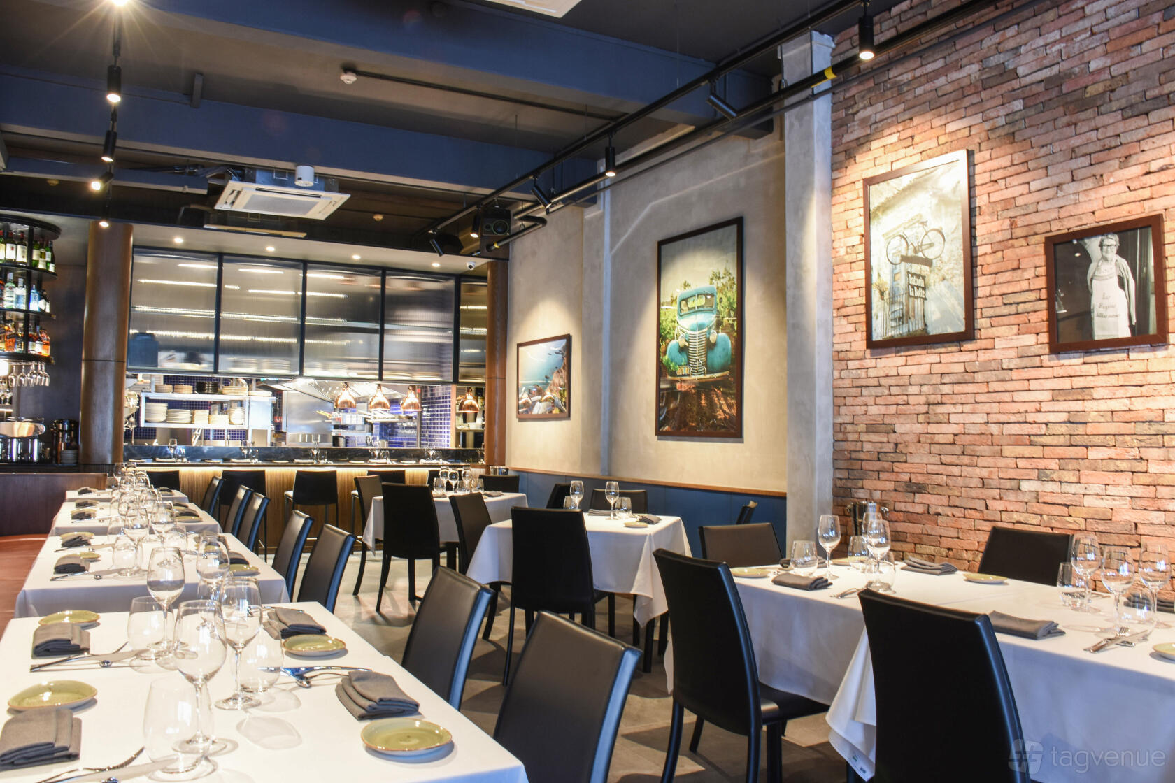 A restaurant with exposed brick walls, framed artwork, and tables set with white linens at Guccio Ristorante.