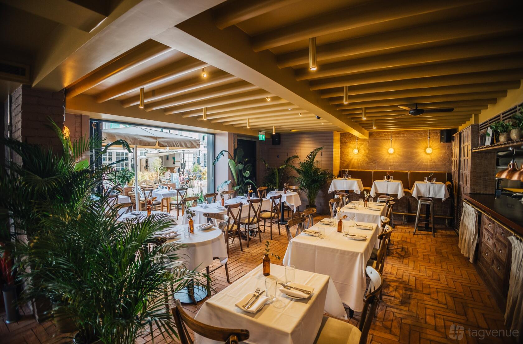 A restaurant with white tablecloths, wooden chairs, brick flooring, and potted plants at PYRÁ.