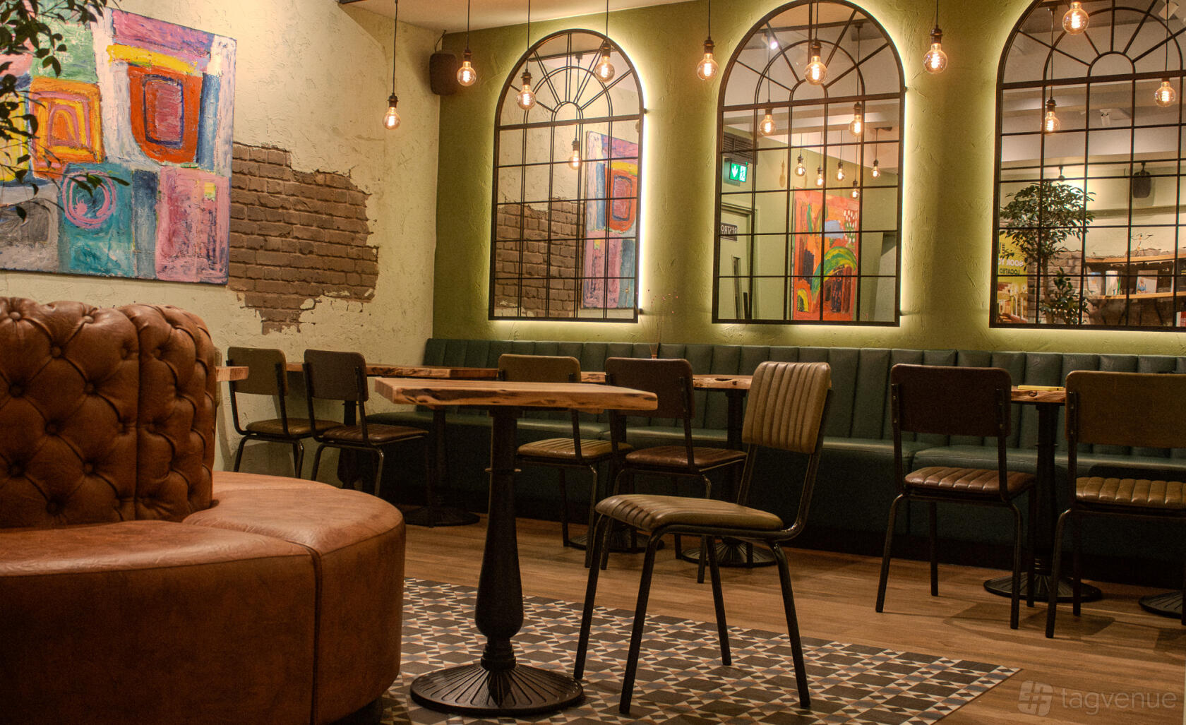 An event space in a restaurant with exposed brick walls, industrial pendant lights, and colorful abstract art at The Veg Box Cafe.
