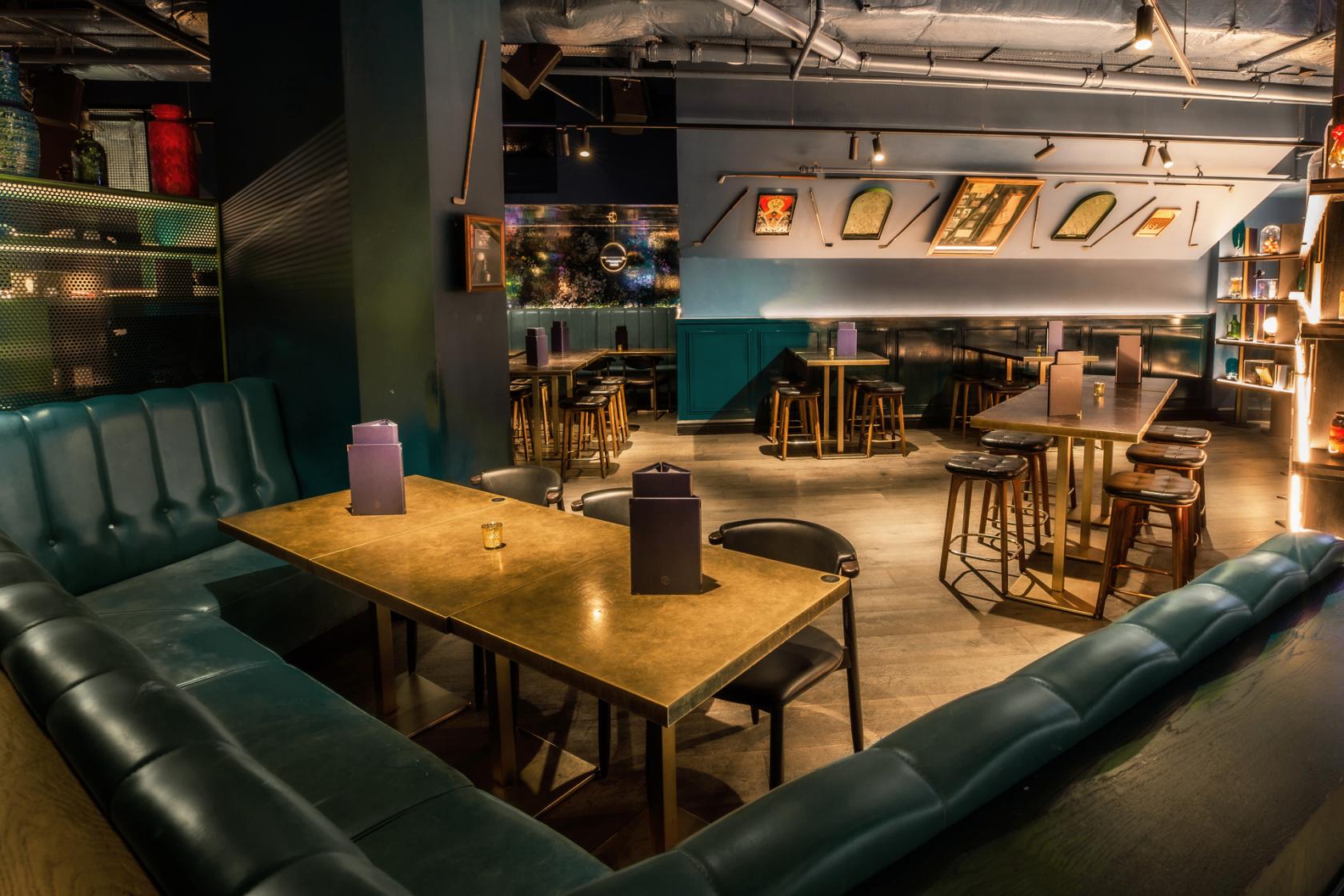 An event venue with teal leather banquette seating, high tables, and ambient lighting at Puttshack Bank.