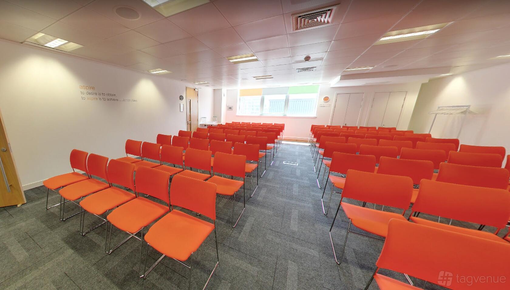 A conference centre with rows of orange chairs, carpeted floor, and large windows at The Studio Glasgow.