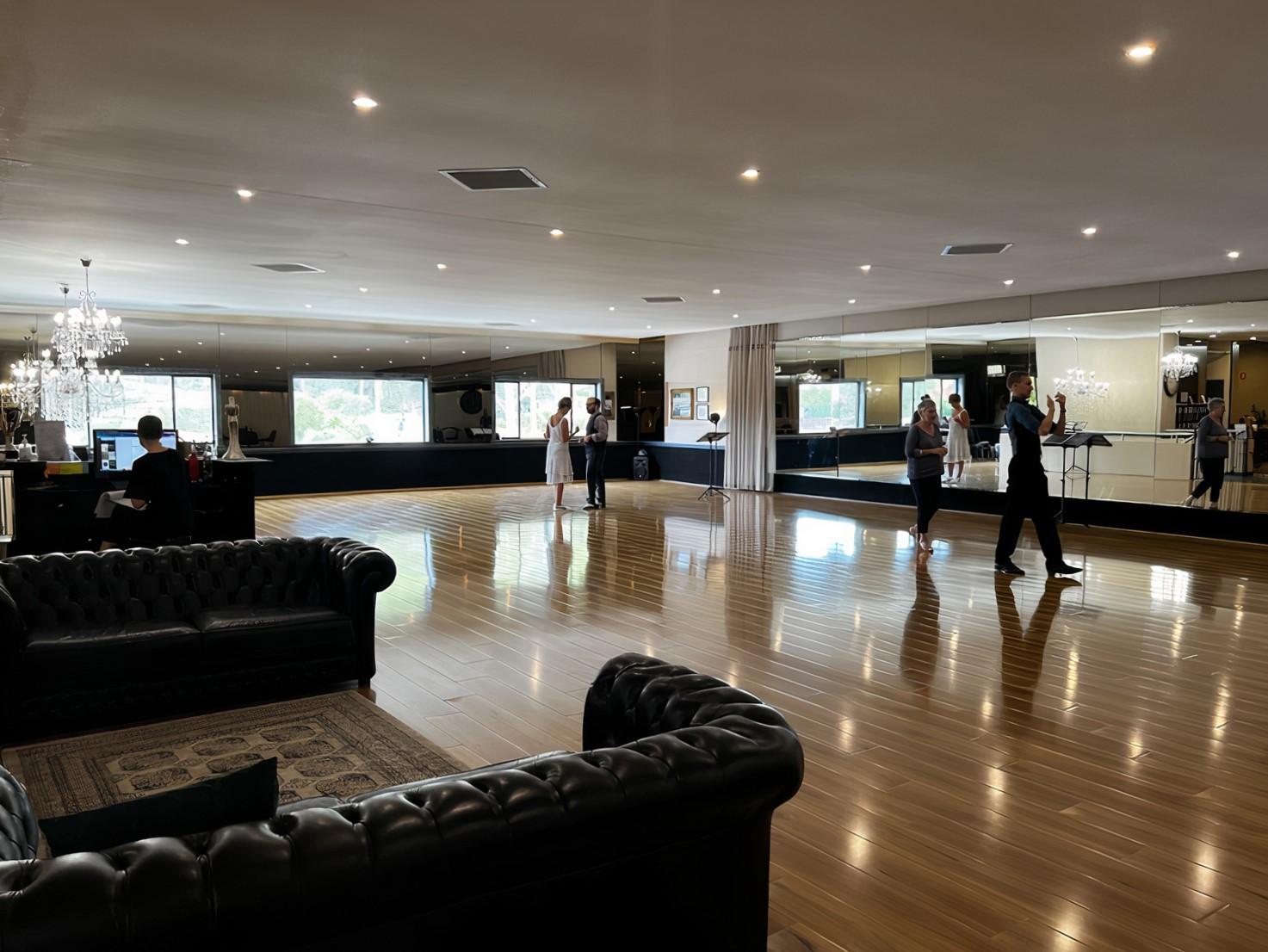 An event venue with polished wood floors, mirrored walls, chandeliers, and black leather sofas at Arthur Murray Inner West.
