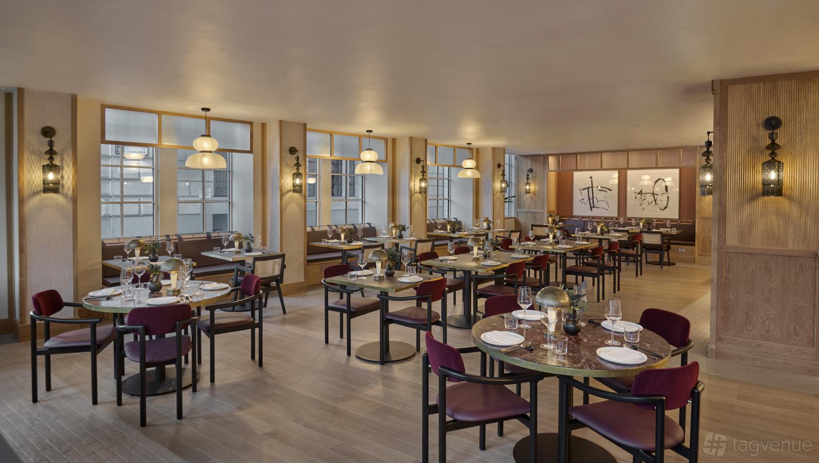 A restaurant dining area with round tables, burgundy chairs, pendant lighting, and large windows at Hyatt Regency London Blackfriars.