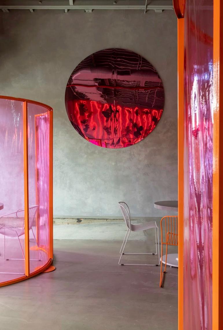 An event space in a bar with translucent pink partitions, metal chairs, and a large red mirrored wall art at Wandering Barman.