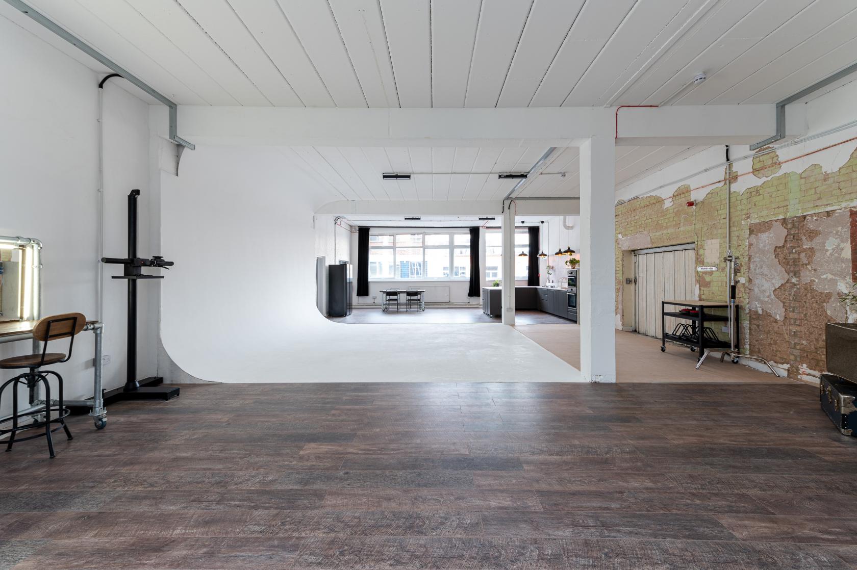 A photo studio with a white cyclorama wall, exposed brick, and wood flooring at 69 drops studios.