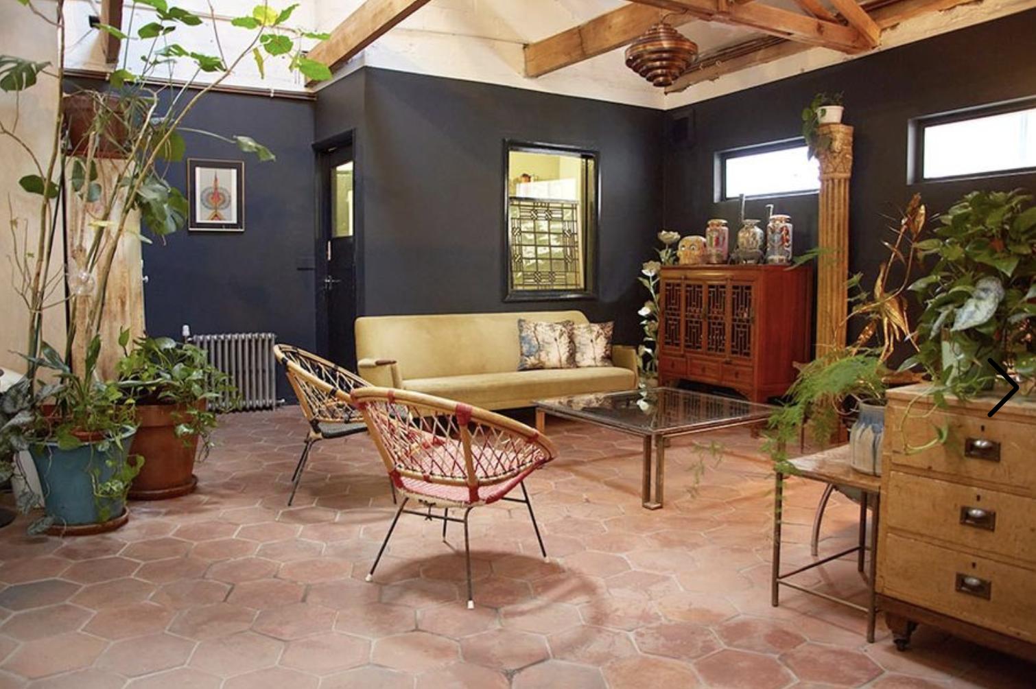 An event space in a photo studio with indoor plants, a yellow sofa, and exposed wooden beams at Apiary Studios Green Room.