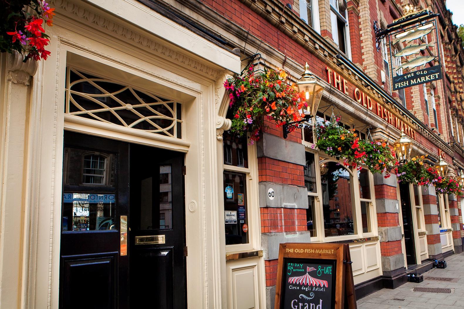 A pub with a red brick facade, hanging flower baskets, and a traditional painted sign at The Old Fish Market.