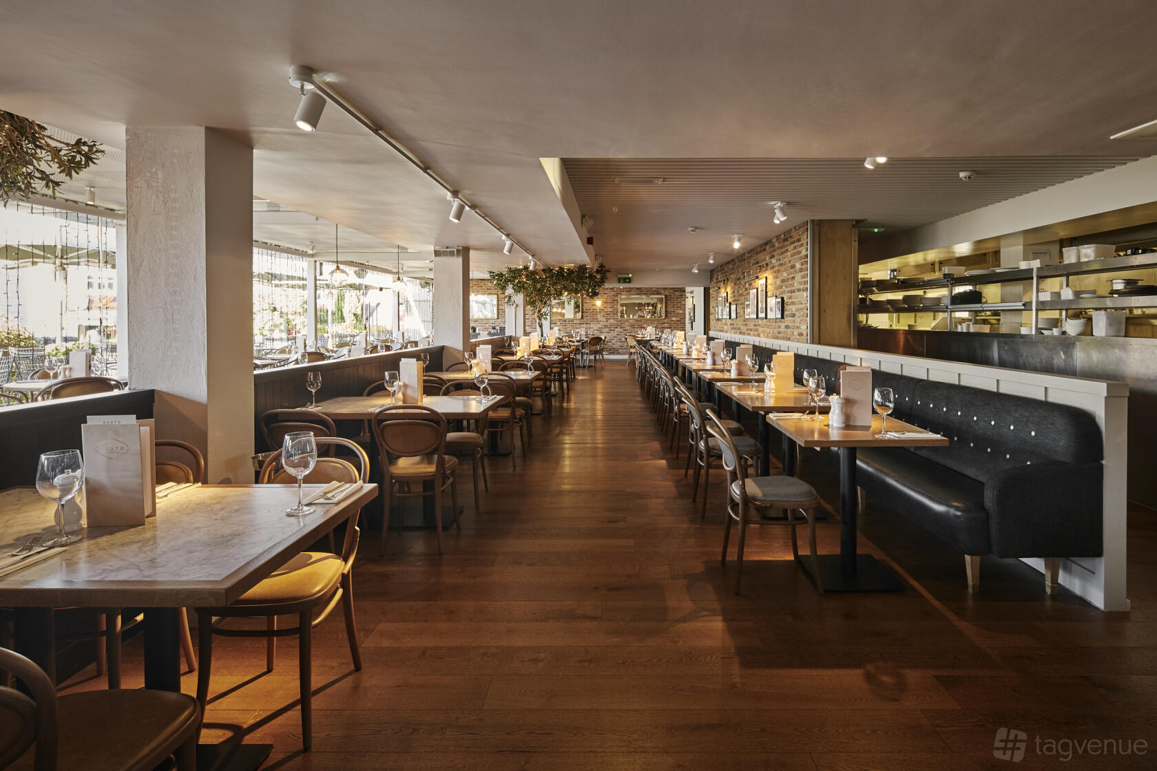 A restaurant with wooden floors, marble tables, banquette seating, and floor-to-ceiling windows at Gusto Italian Cheadle.