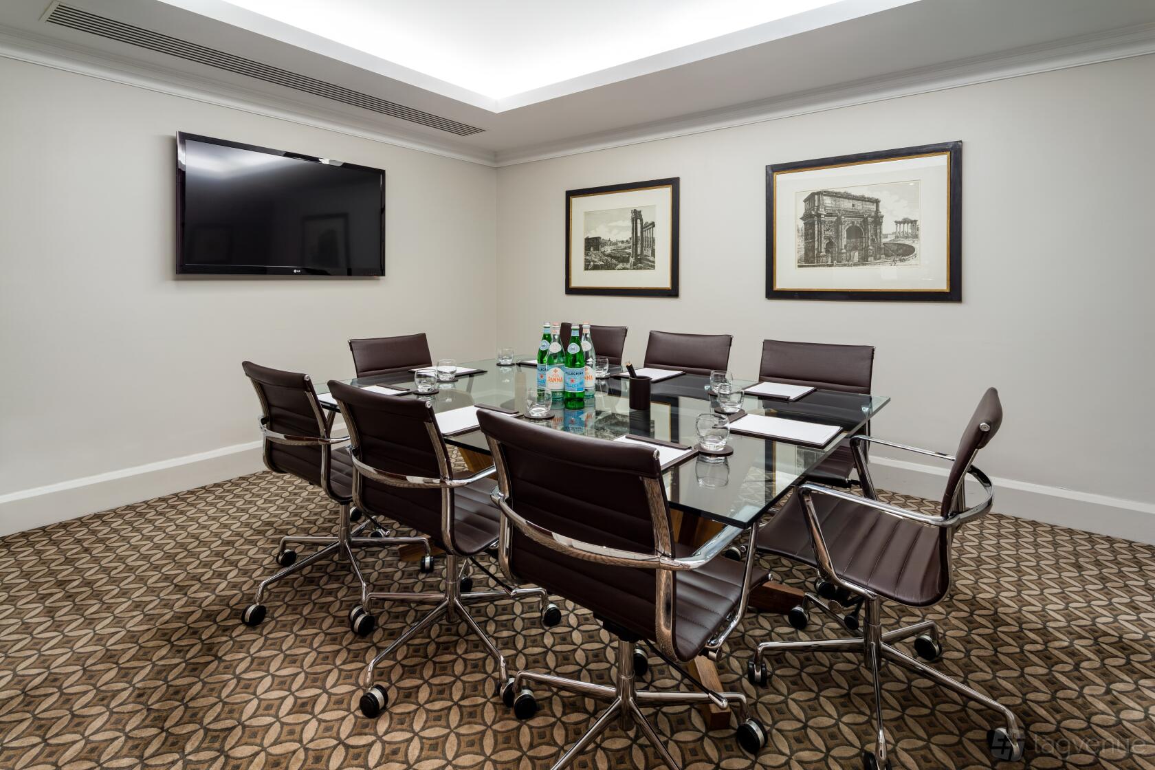 A hotel meeting room with a glass conference table, leather chairs, wall-mounted TV, and framed art at Radisson Blu Hotel, London Euston Square.