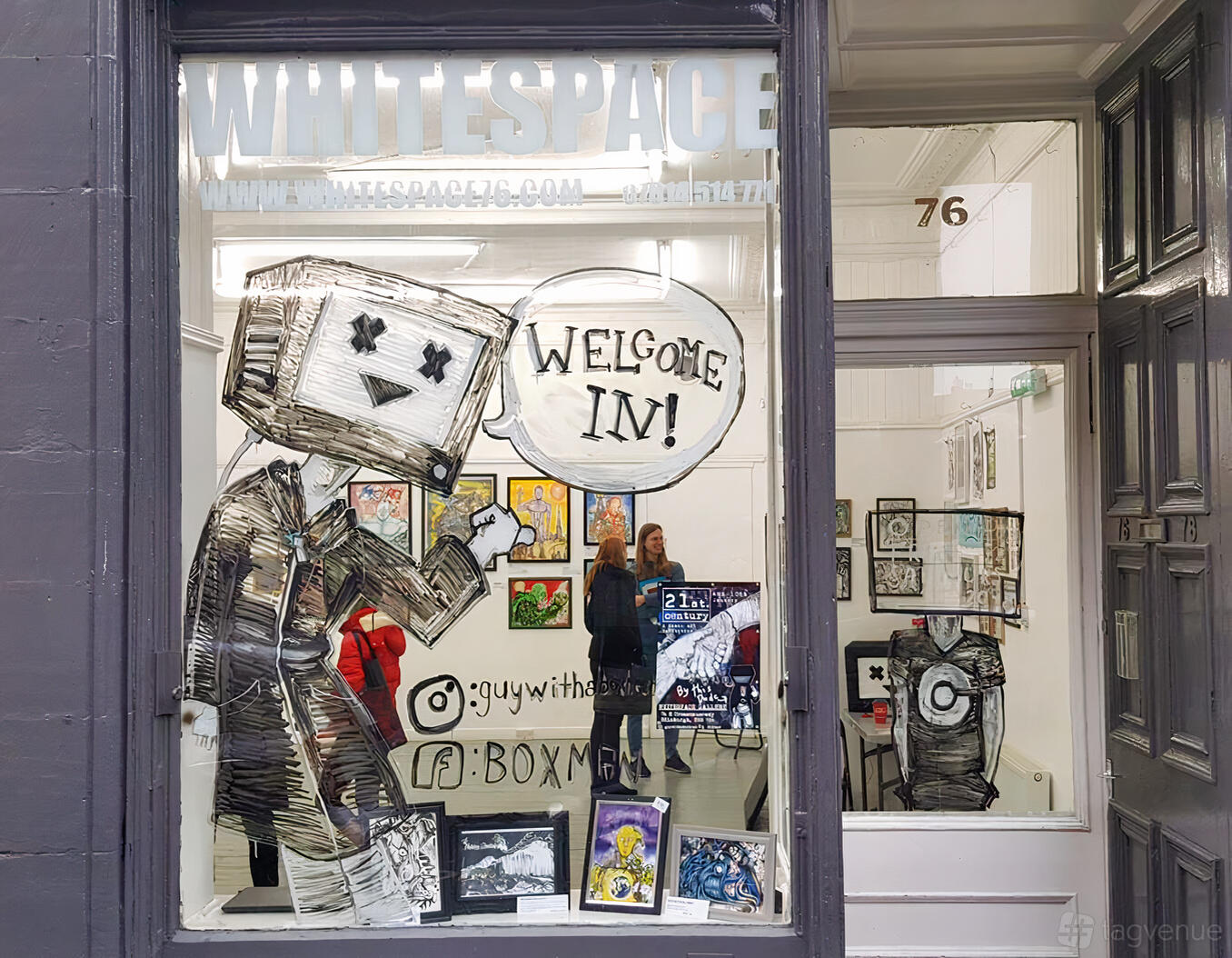A gallery with white walls, eclectic framed artwork, and large illustrated window art at Whitespace Gallery.