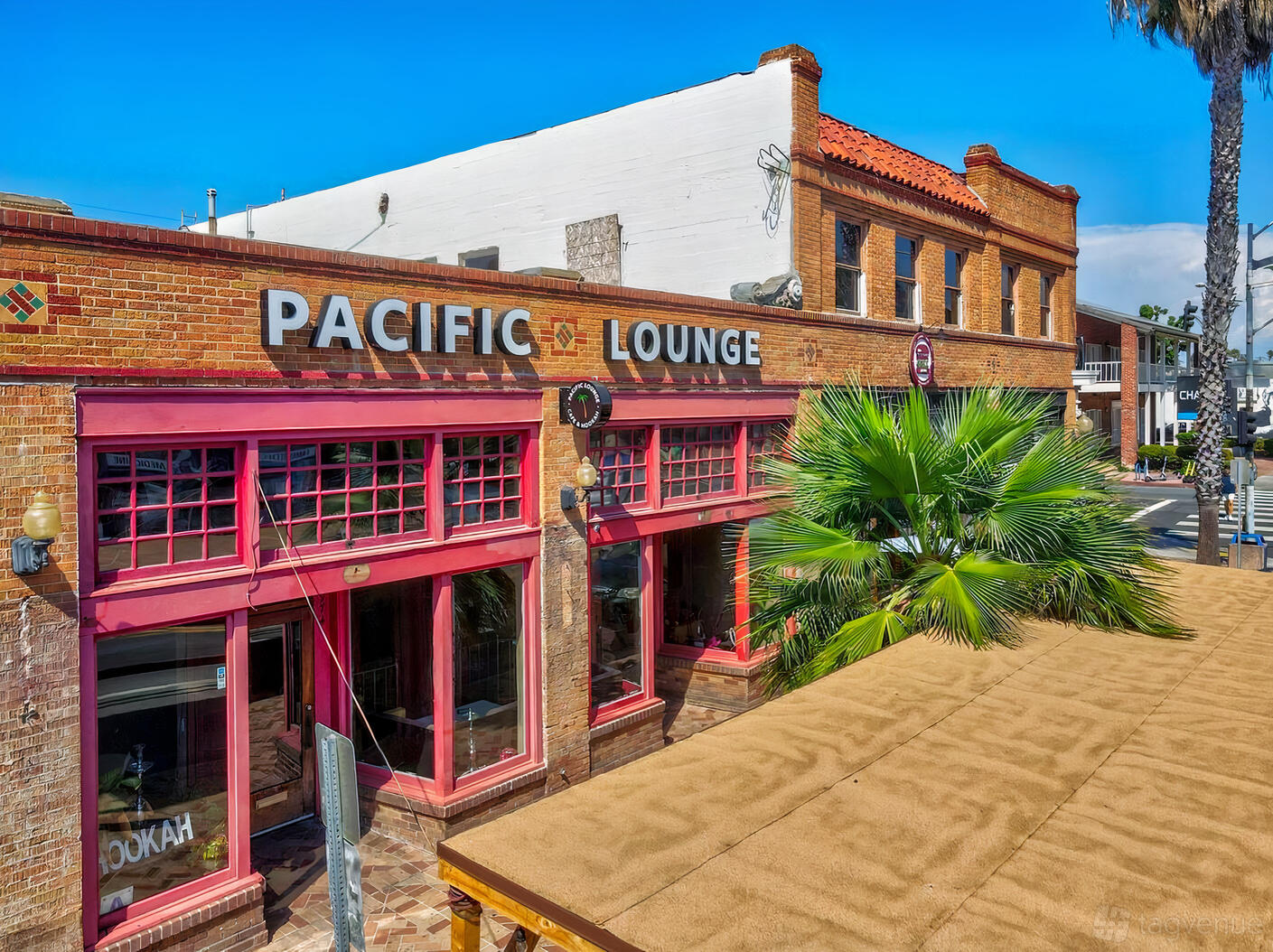 A brick pub with large red-trimmed windows and a palm tree at the Pacific Lounge.