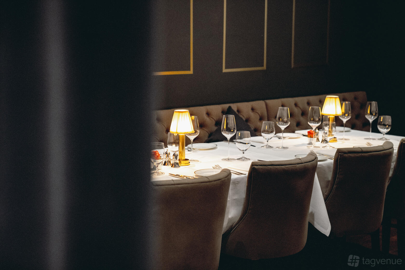 A dining room with a long table, white tablecloth, cushioned chairs, and small lamps at Jamuna.