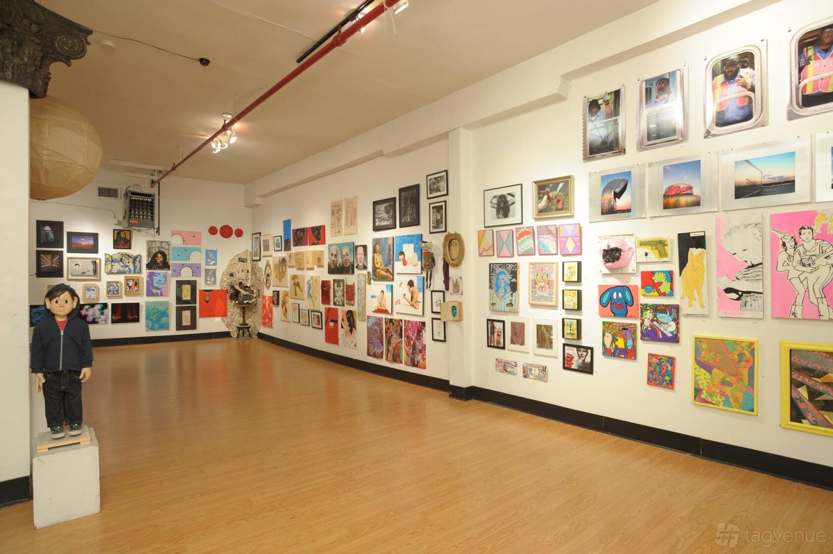 A gallery with hardwood floors and walls covered in colorful artwork at The Greenpoint Gallery.