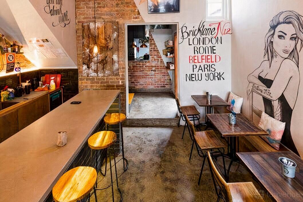 A cafe with exposed brick walls, mural art, wooden stools, and small tables at Bricklane N12.