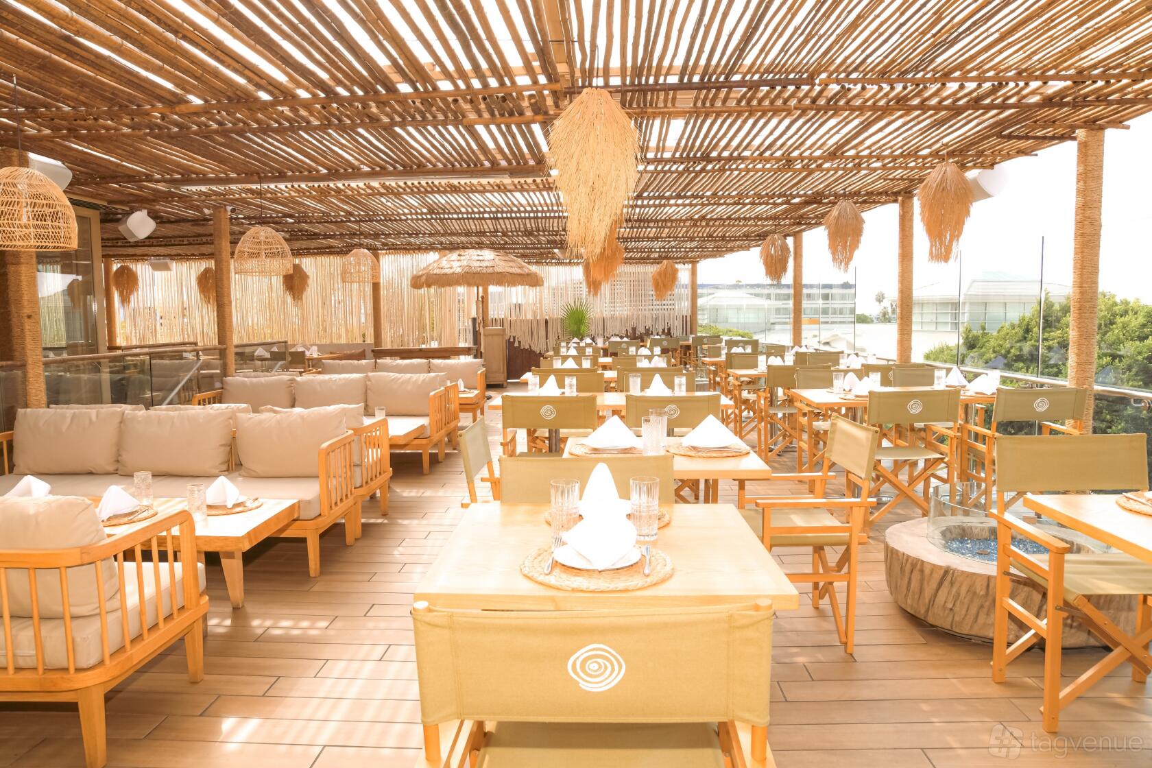A terrace with wooden decking, bamboo overhead covering, cushioned lounge seating, and dining tables at LouLou.