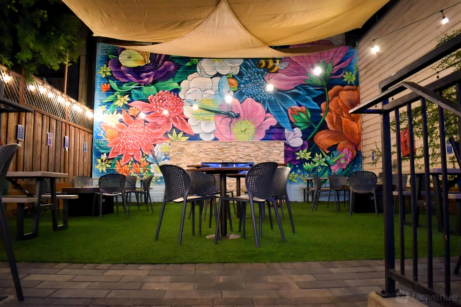 A garden patio with string lights, colorful floral mural, shade canopy, and outdoor seating at Campus.
