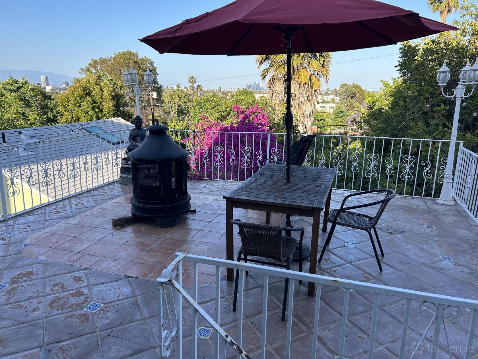 An outdoor venue with a tiled balcony, wooden table and chairs, umbrella, and garden view at LA Manor.