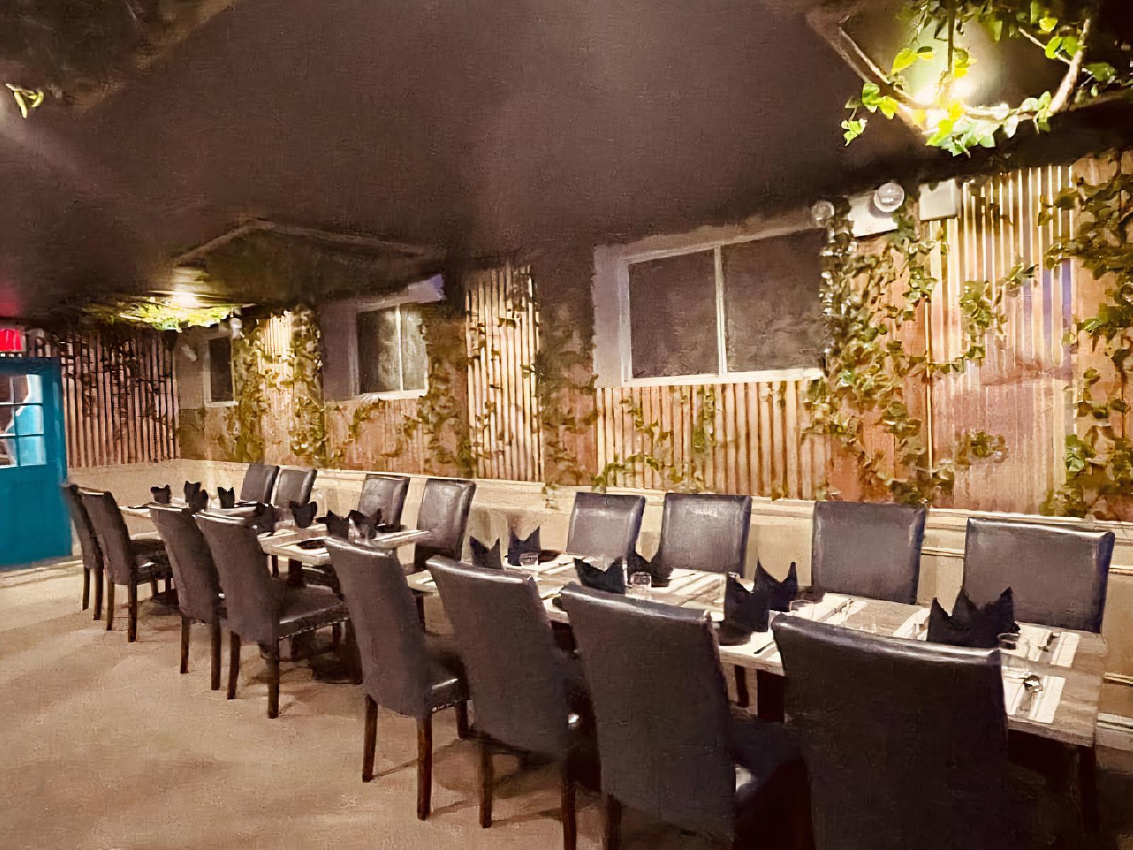 A restaurant with a long table set with black napkins and greenery climbing wood-panel walls at Aanch Indian & Indo Chinese Restaurant.