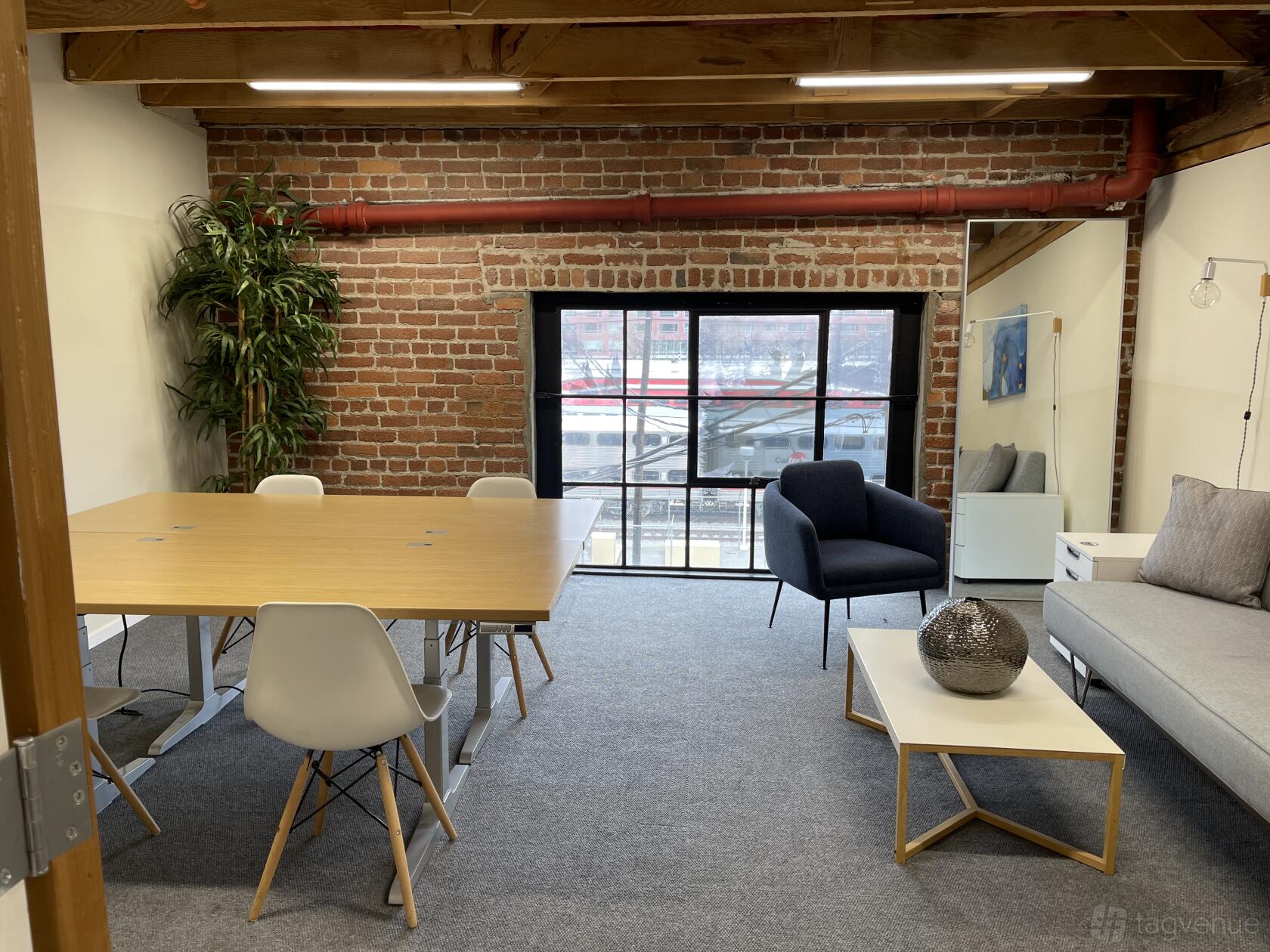 A meeting room with exposed brick walls, a wooden ceiling beam, and a large window at 350 Townsend.