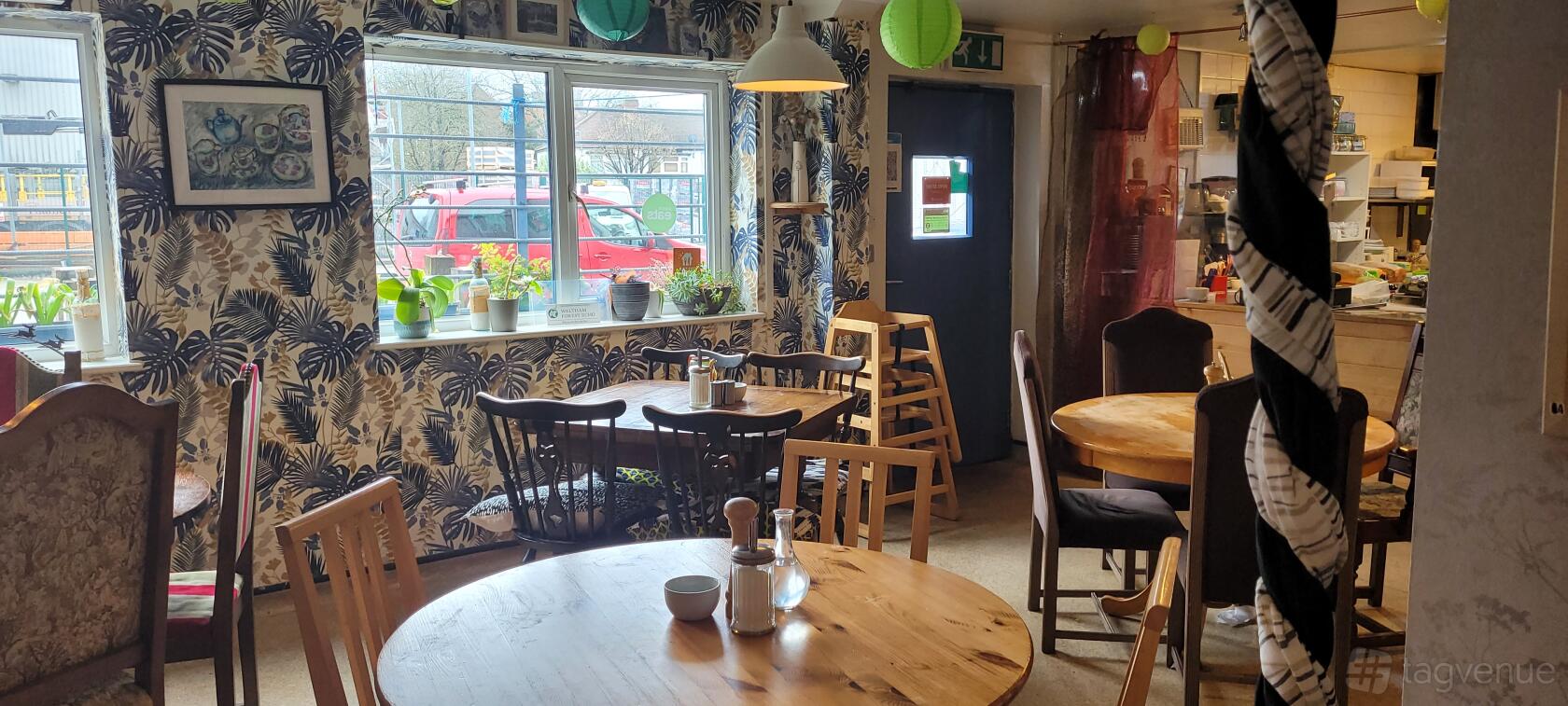 A cafe with round wooden tables, mismatched chairs, potted plants on the windowsill, and patterned wallpaper at Old Station Yard Cafe.