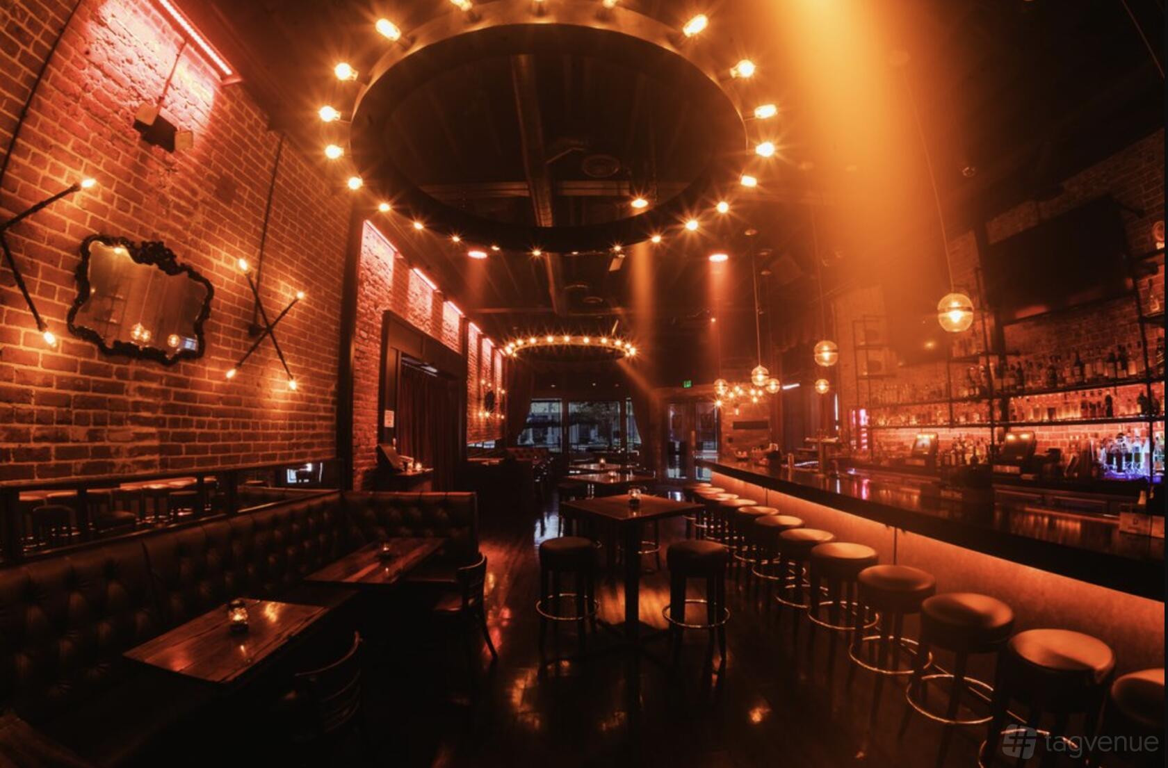 A dining room with exposed brick walls, tufted leather seating, and circular chandeliers at ProAbition - Riverside.