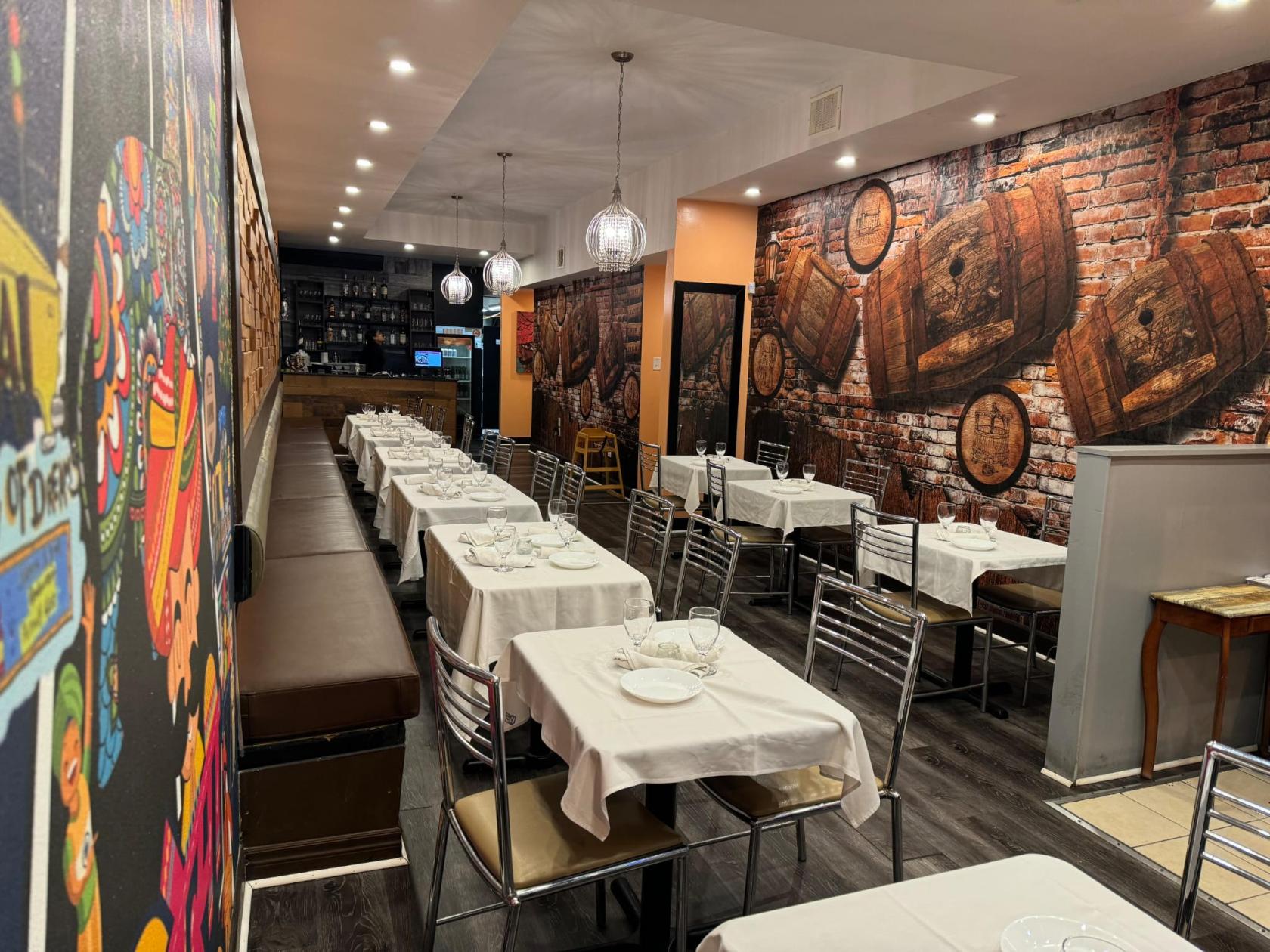 A restaurant dining room with white tablecloths, metal chairs, and mural-covered brick walls at Namaste Indian Cuisine.