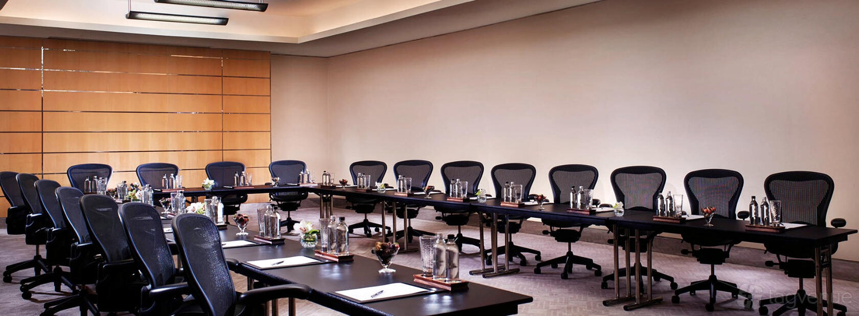 A meeting room with ergonomic chairs, long tables arranged in a U-shape, and bottled water at Pan Pacific Singapore.
