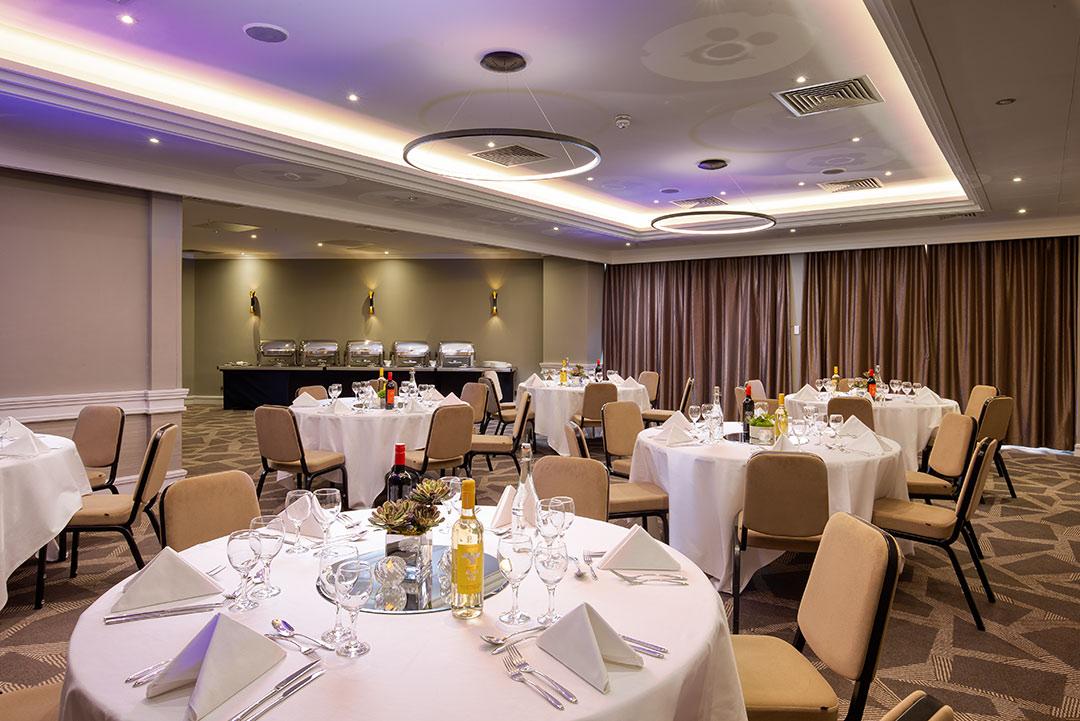 A hotel banquet room with round tables set with white linens and a buffet setup at DoubleTree by Hilton London - Ealing.