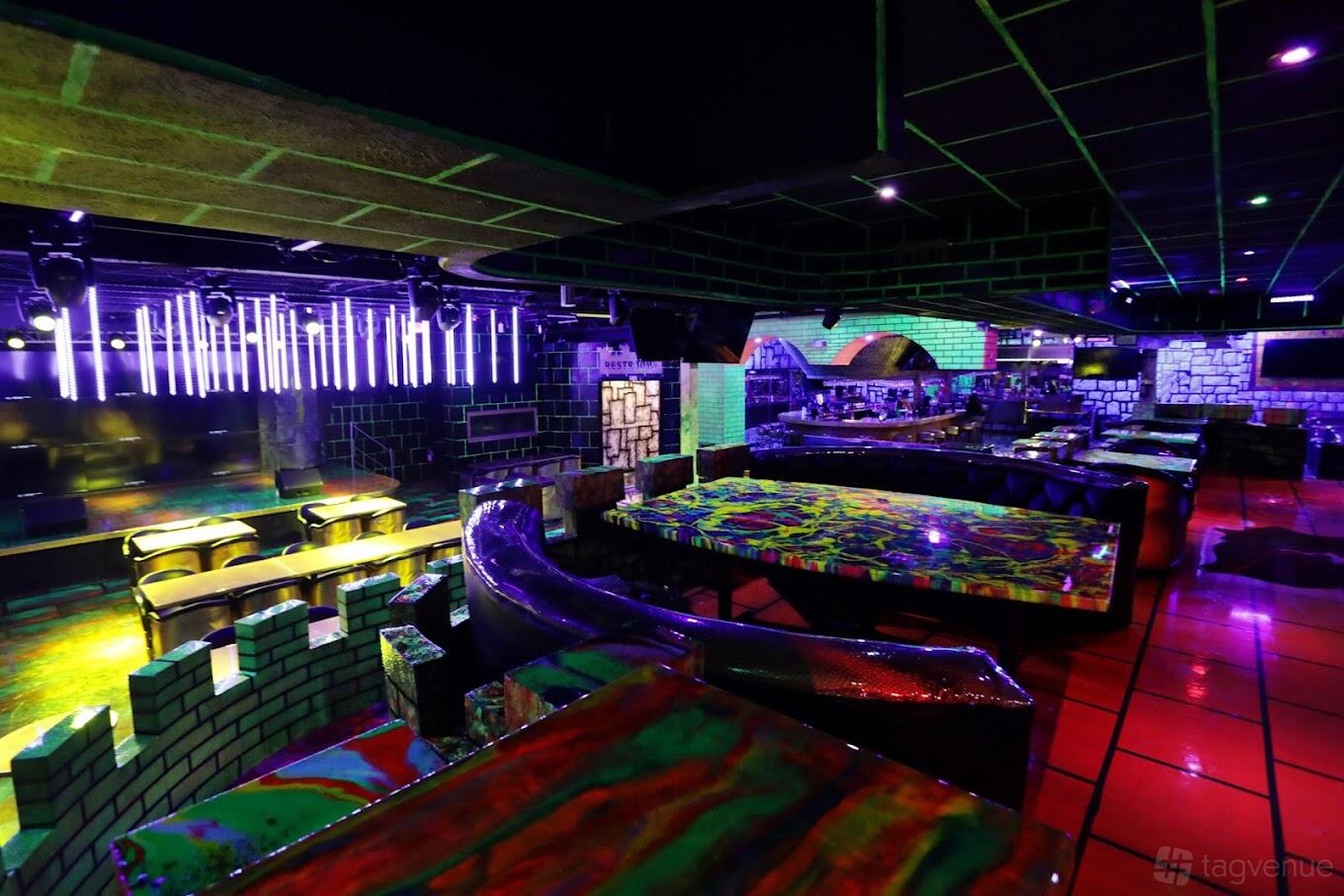A bar with neon lighting, painted brick walls, and colorful marble-effect tables at The Castle Lounge.