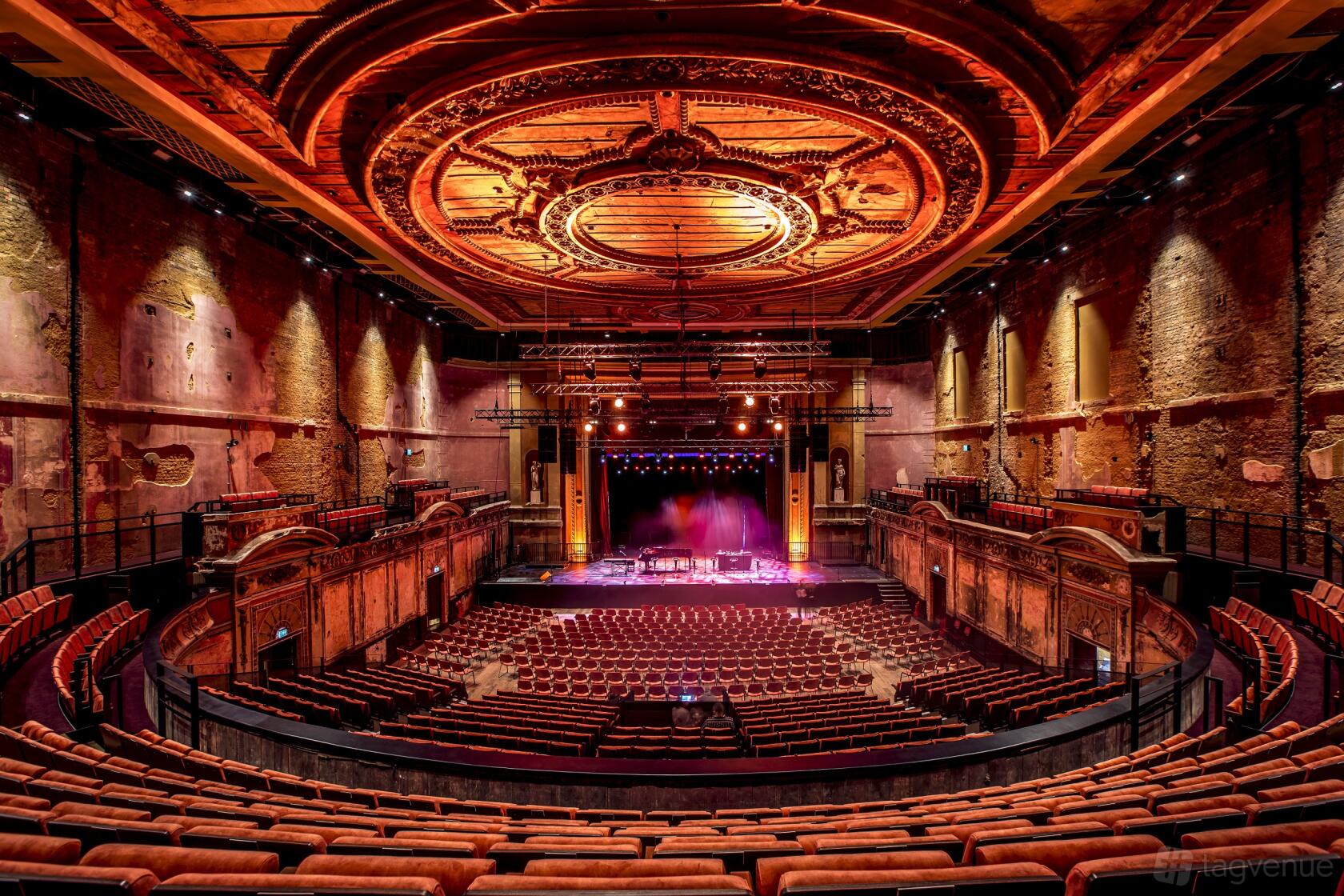 An auditorium with ornate domed ceiling, exposed historic walls, and tiered seating at Alexandra Palace Victorian Theatre.